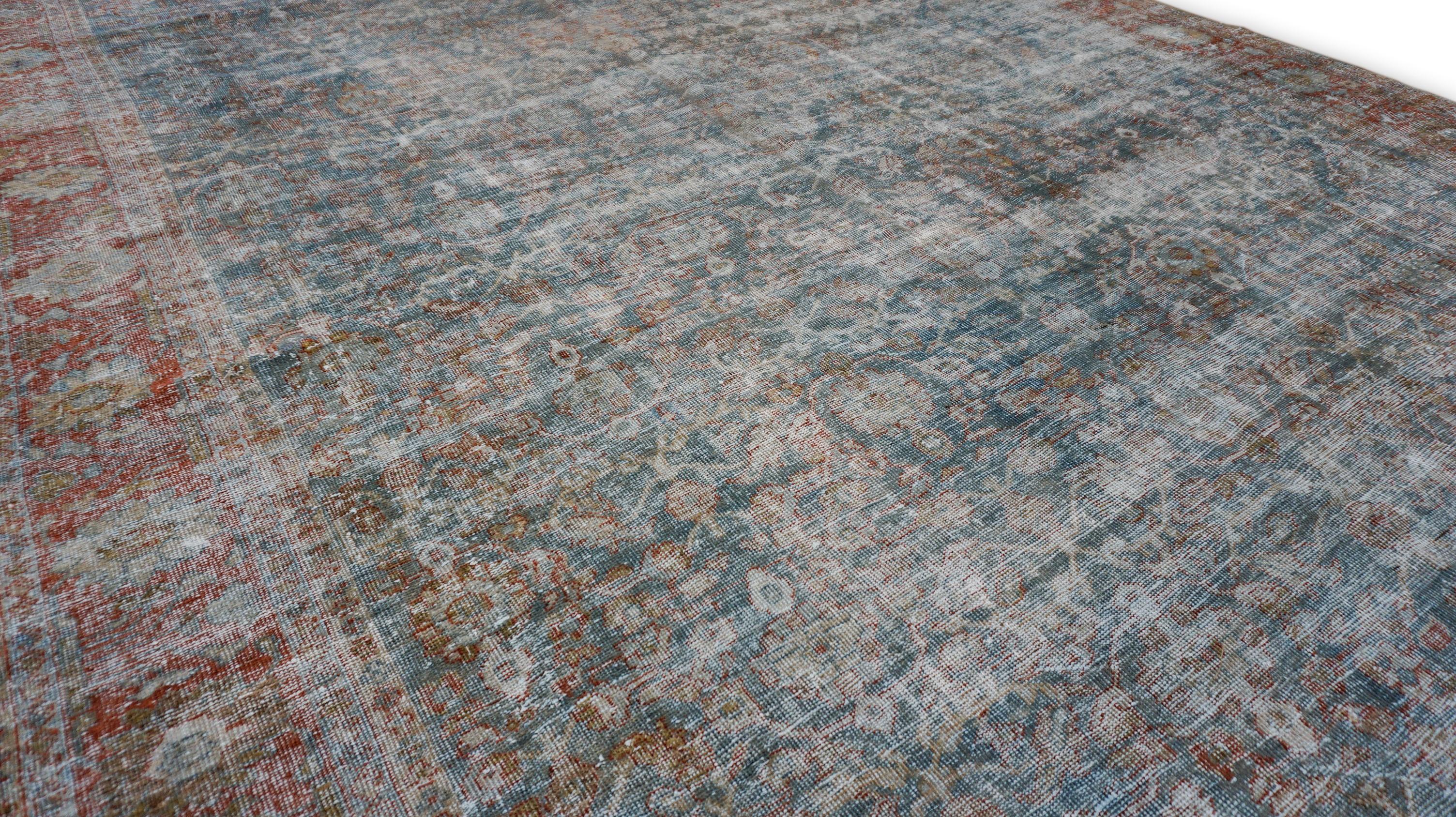 Dieser antike, handgeknüpfte Wollteppich weist ein zart verblasstes florales und geometrisches Muster auf und strahlt eine zeitlose Eleganz aus, die von seiner reichen Geschichte zeugt. Das sanfte, gedämpfte blaue Feld mit roter/rostfarbener