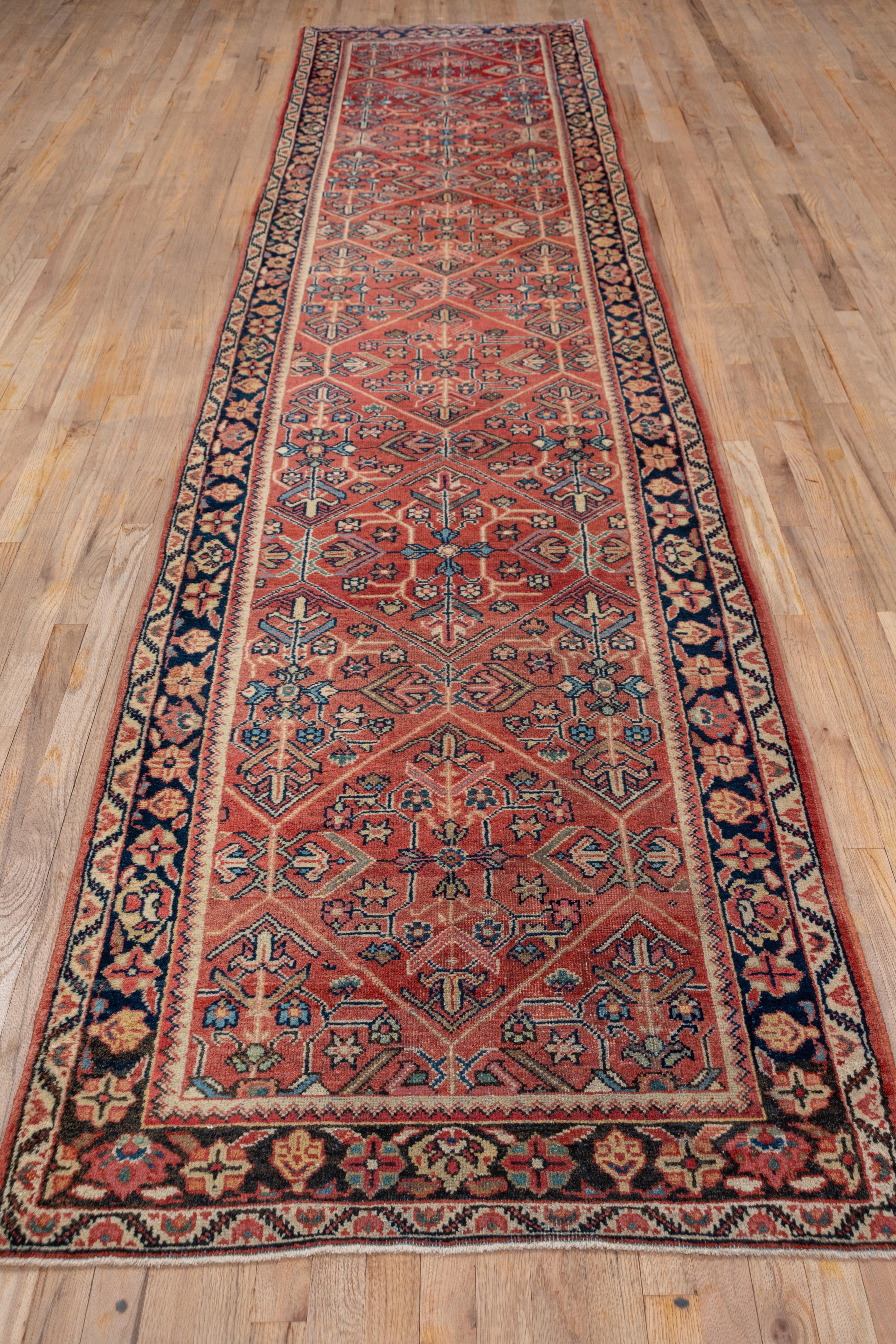 The soft ground displays a large open hexagonal lattice pattern enclosing four palmette cruciforms detailed in light blue, ivory and navy. There is a simple navy border of winged rosettes and palmettes on this west Persian village runner. The