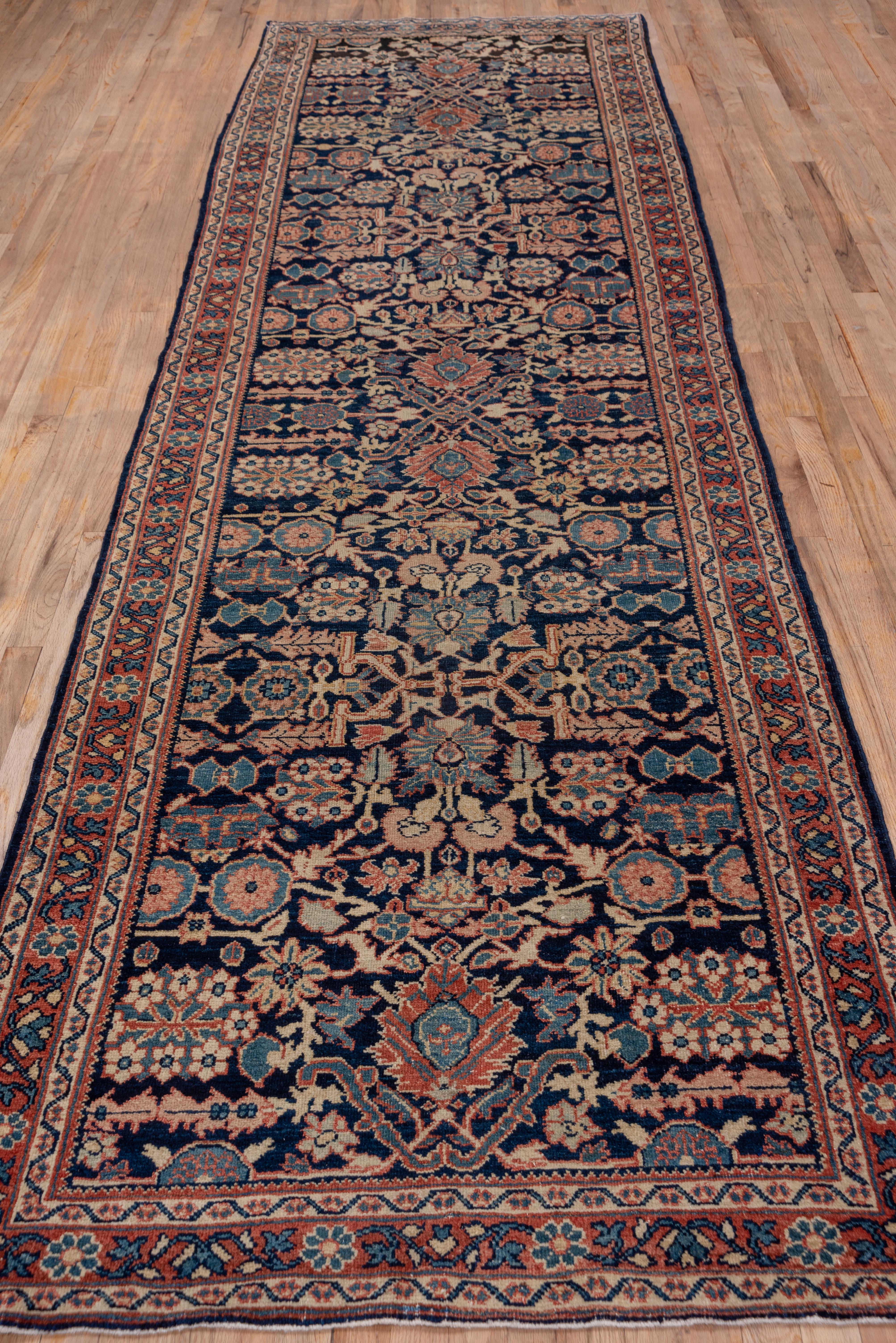 This west Persian village runner shows a deep blue field with secondary touches in lighter blues, decorating a centrally organised palmette pattern with round and petal rosettes and thick arabesques in blue and cream. The narrow madder border shows