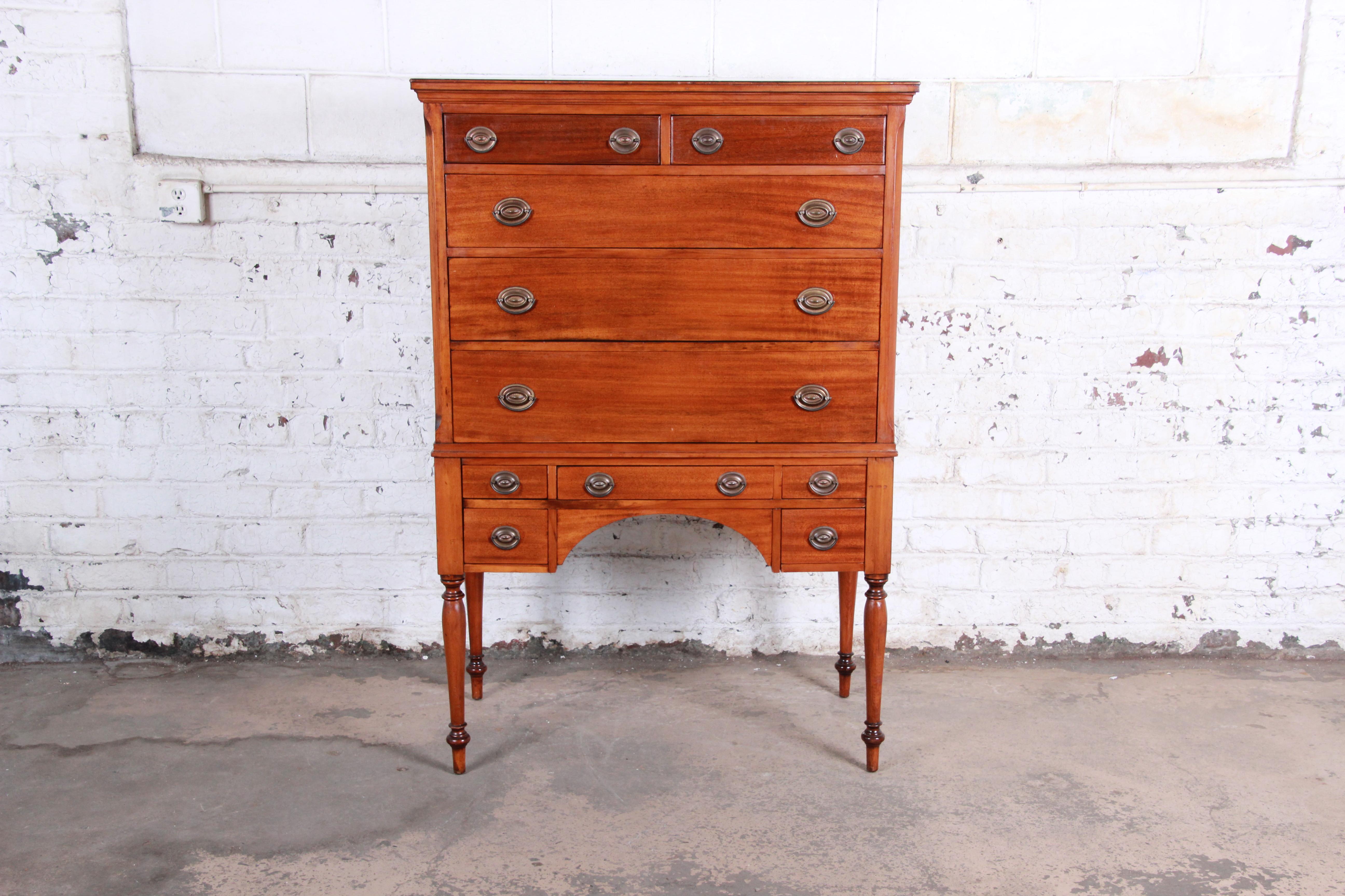 A gorgeous antique mahogany highboy chest by Estey Manufacturing Co. of Owosso, MI. The dresser features stunning mahogany wood grain and a nice traditional colonial style. It offers ample storage, with ten dovetailed drawers. The chest sits on