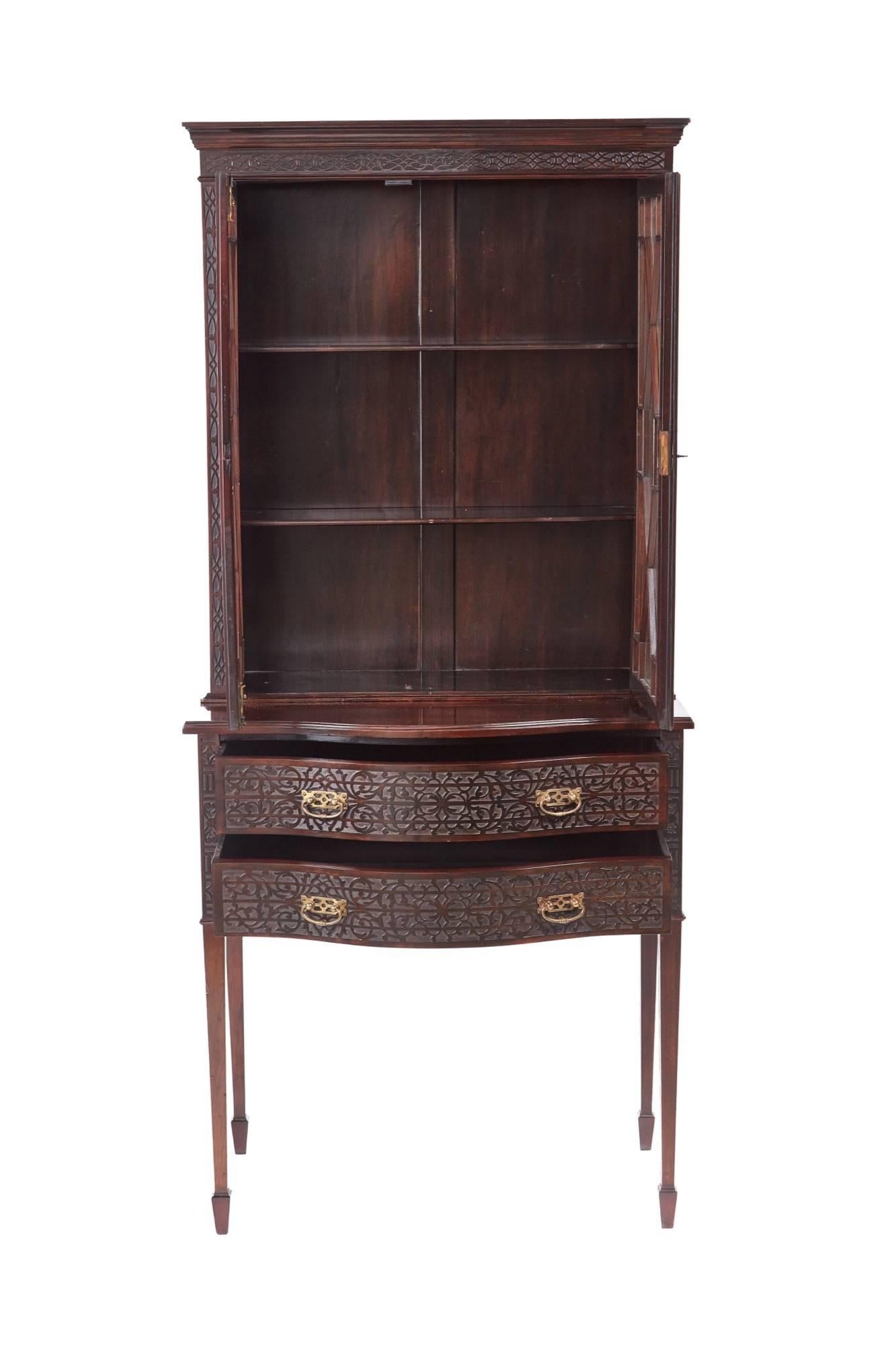 Antique mahogany blind fret display cabinet, with a shaped cornice blind fret frieze, two astragal glazed doors opening to reveal two adjustable shelves, the base having two serpentine shaped blind fret drawers with original brass handles, supported