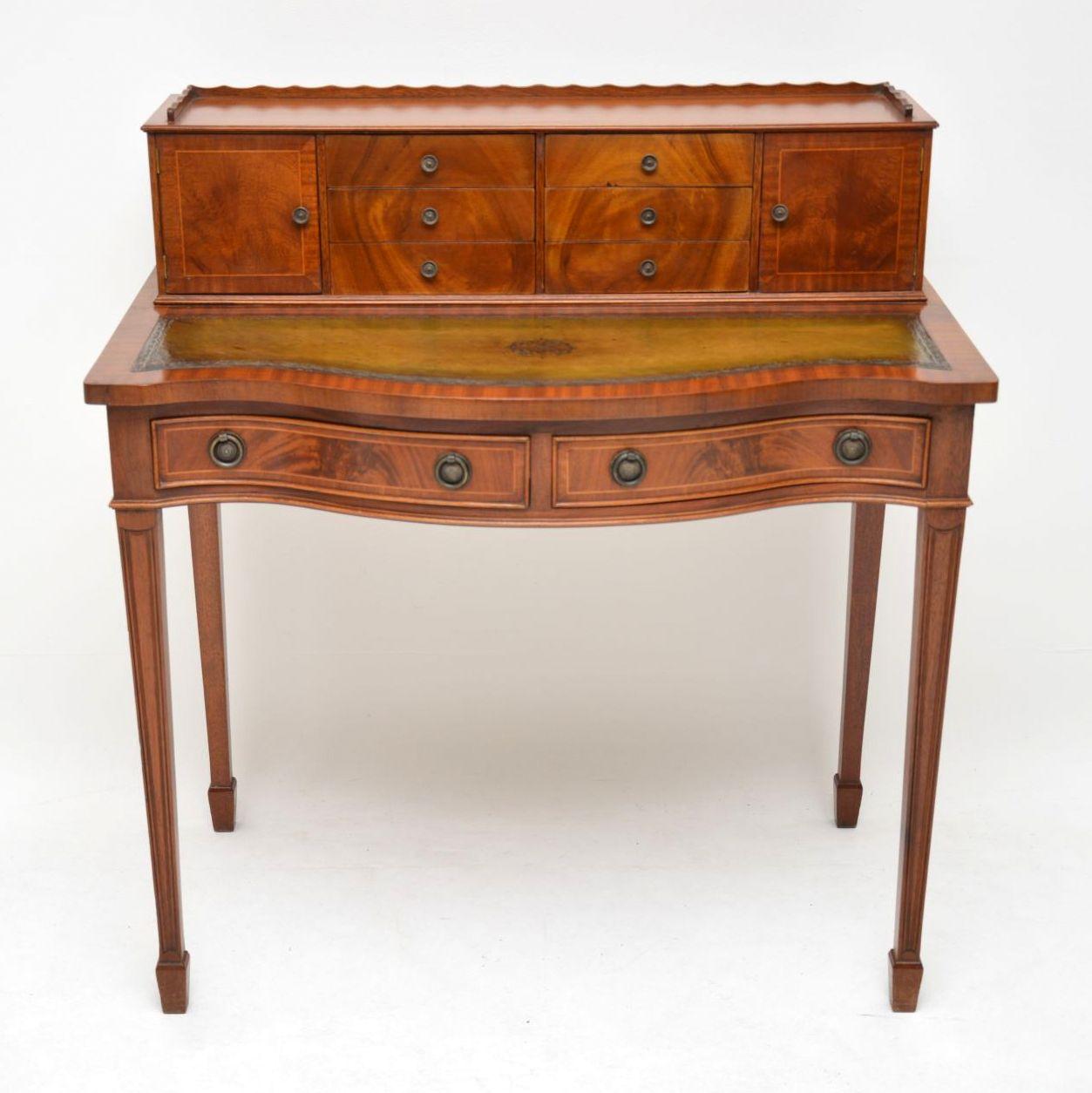 This antique Sheraton style flame mahogany writing table is in excellent condition and dates to around the 1950s period. It has a serpentine shaped front with two drawers and a high superstructure with cupboards and small drawers. The flame mahogany