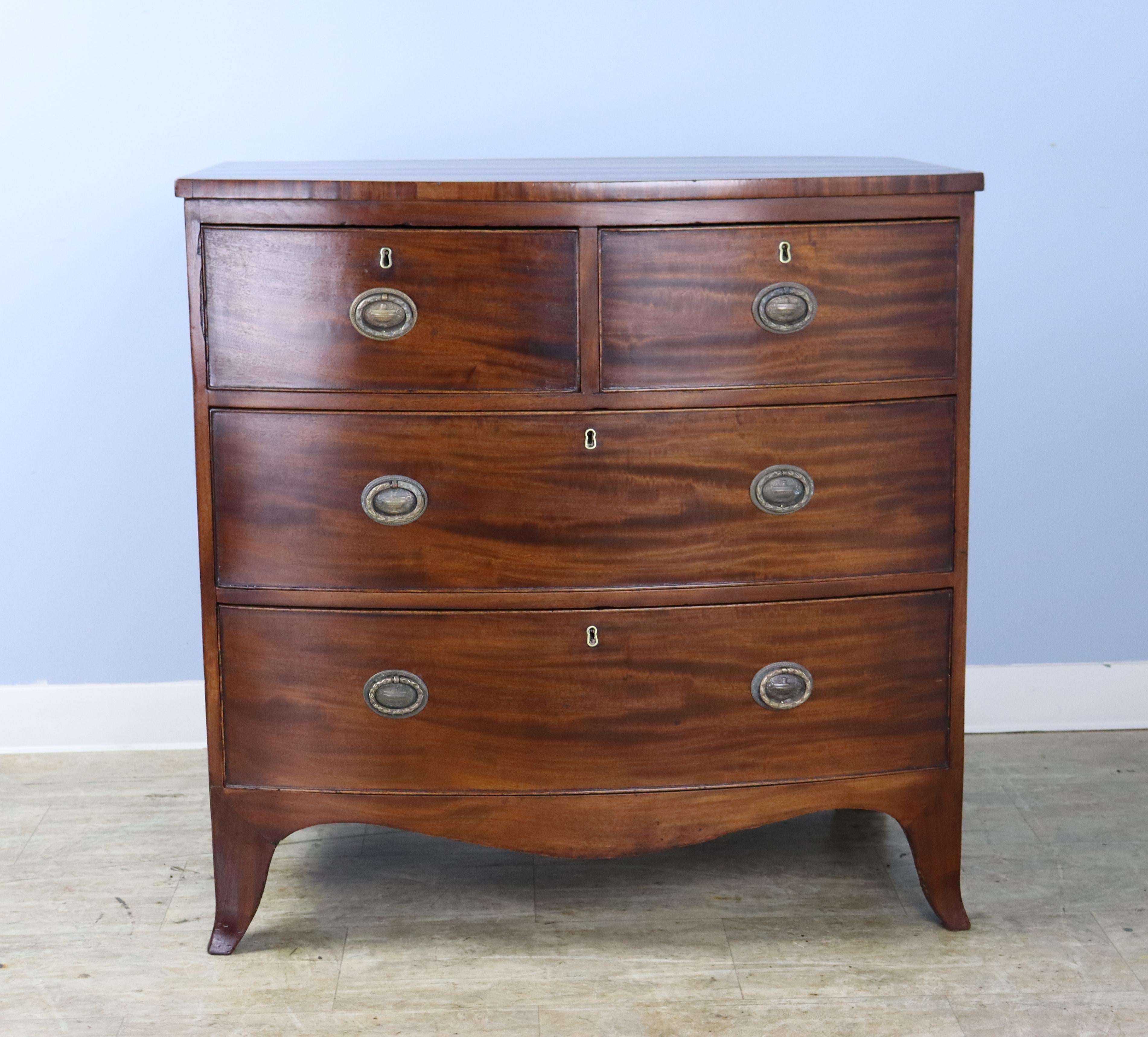 An elegant smaller antique bowfront bureau. The mahogany is a rich medium color with a lovely grain. Details of note include the cockbeading on the drawers, and beautifully wrought brass drawer pulls. The graceful French style feet are original.