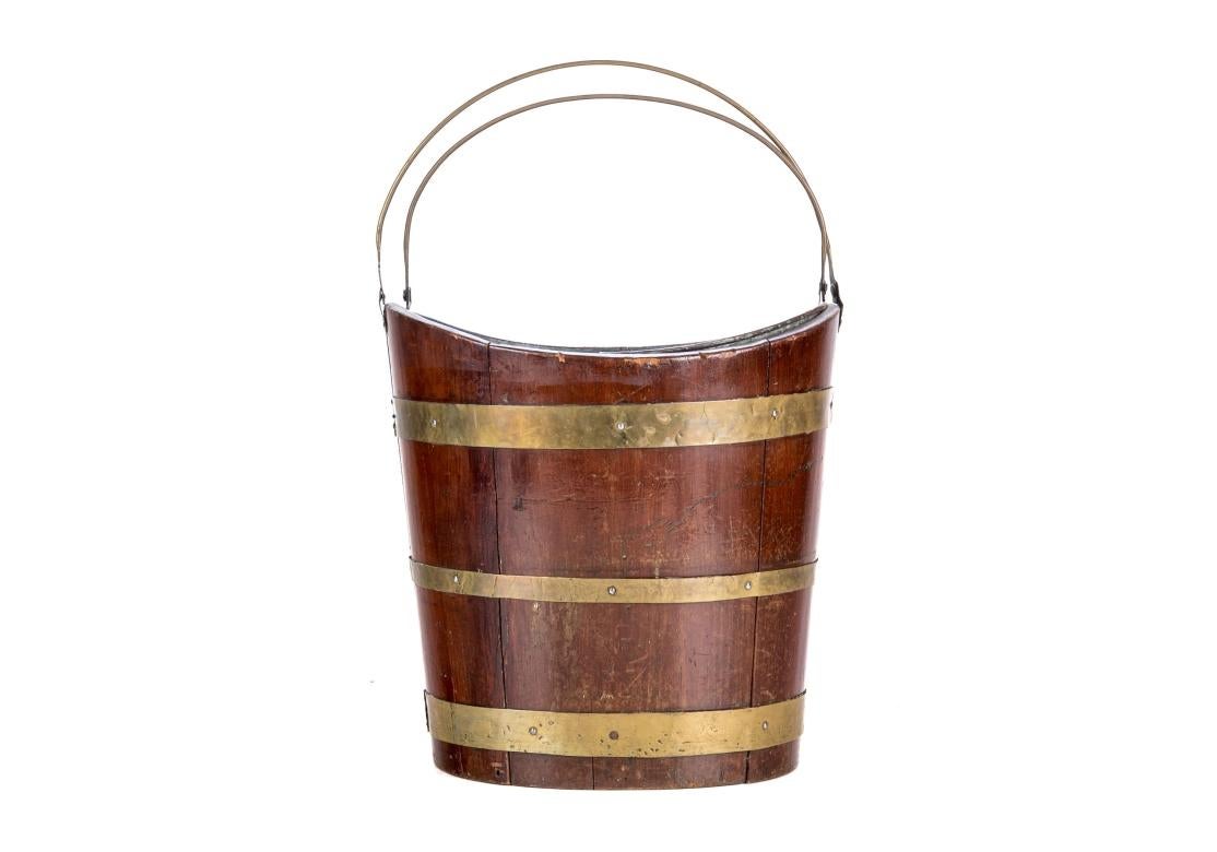 Antique mahogany peat bucket with slope front and back, brass banded, retracting brass handle and a conforming galvanized liner with matching brass handle. Unmarked.

Dimensions: 12 3/4
