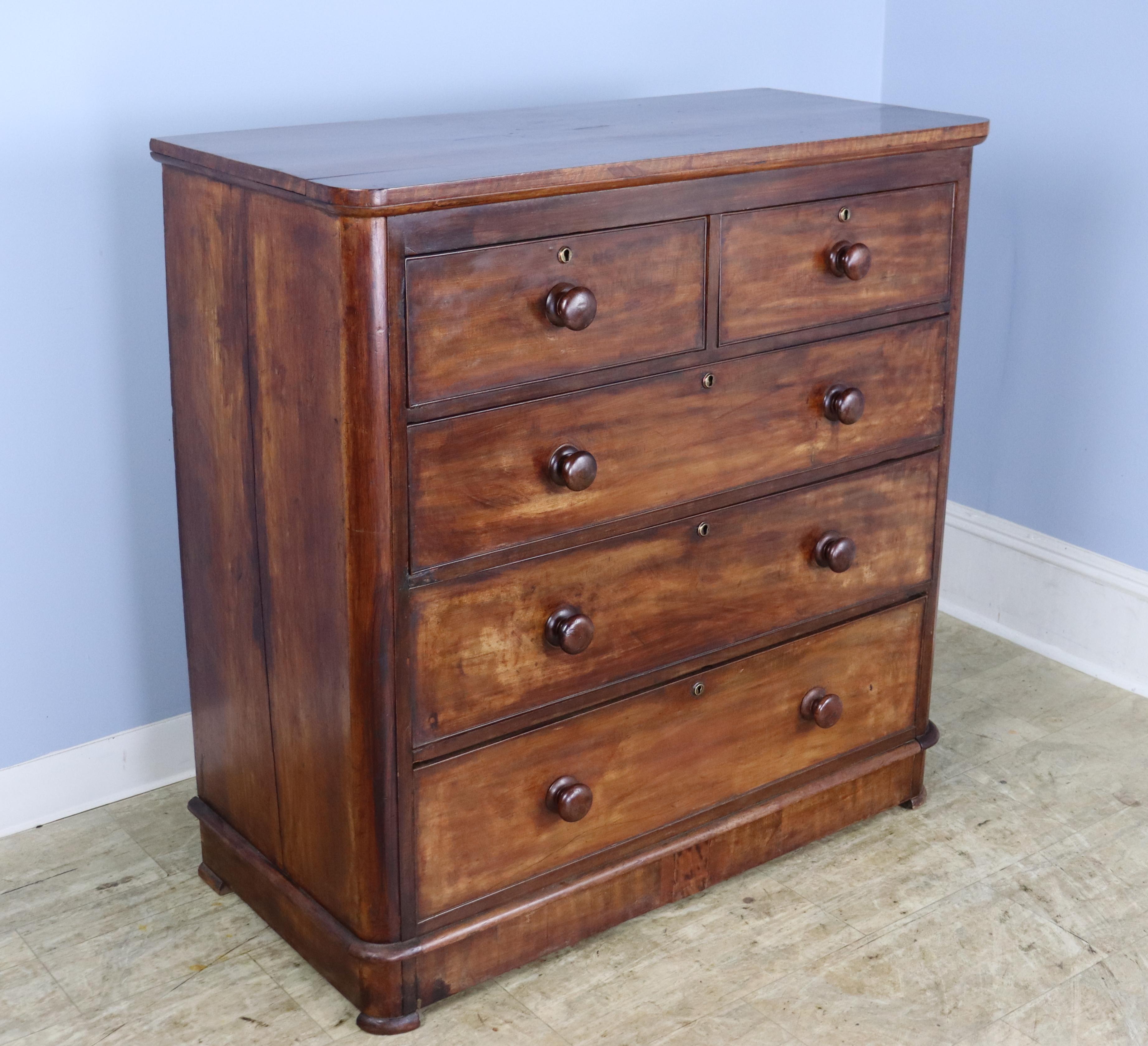 A large chest of drawers in rich mahogany, with very deep drawers and stylish glossy knobs.  The plinth at the bottom opens with the bottom drawer, a fun detail.  The brass keyholes are original although there are no keys.  There is some light wear