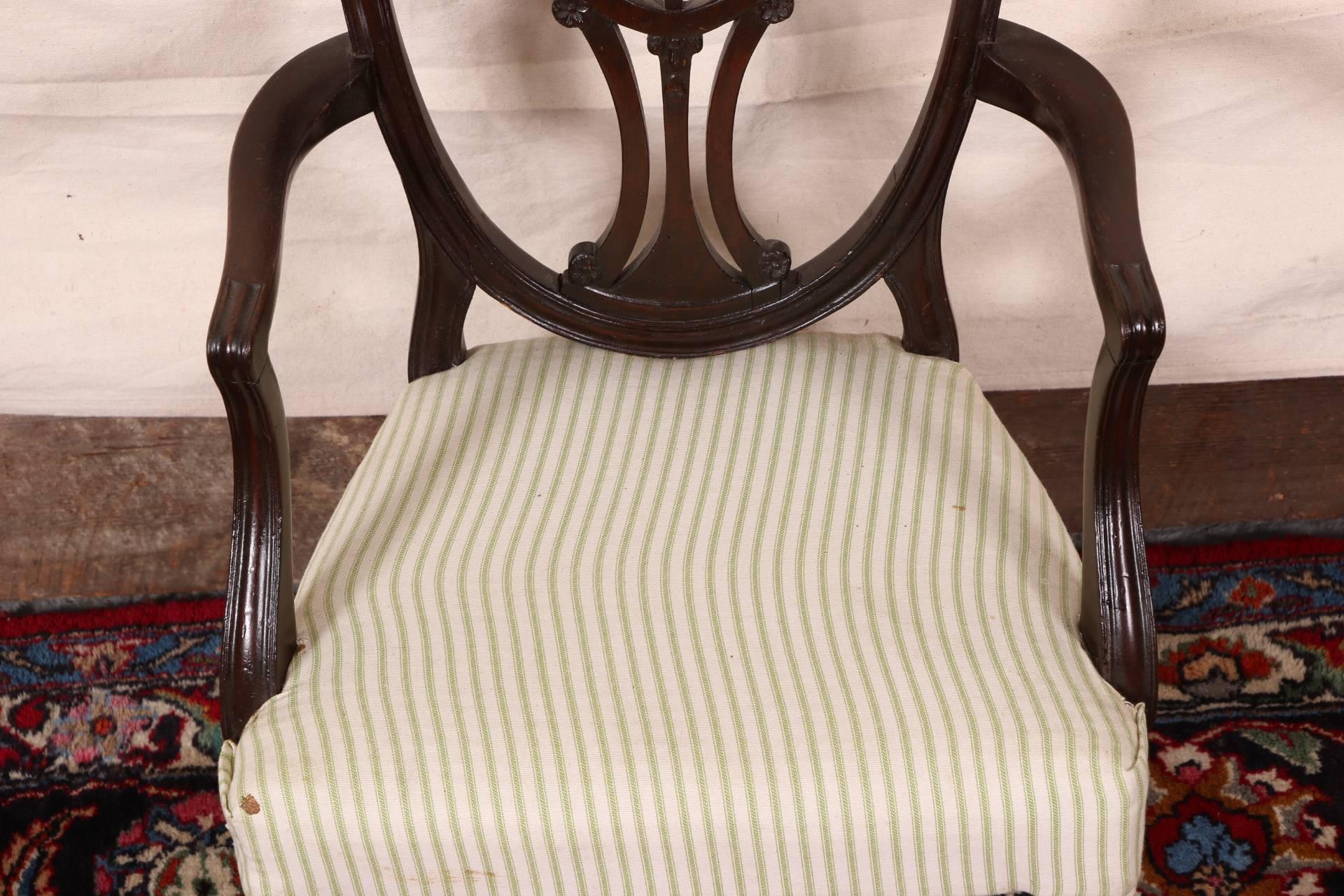 With a shaped crest rail and openwork splat back with wheat sheaf motif at the top. With curved arms, and raised on square front legs with spade feet and splayed back legs. Green and white striped seat upholstery.
Condition: Wear to crest rail,