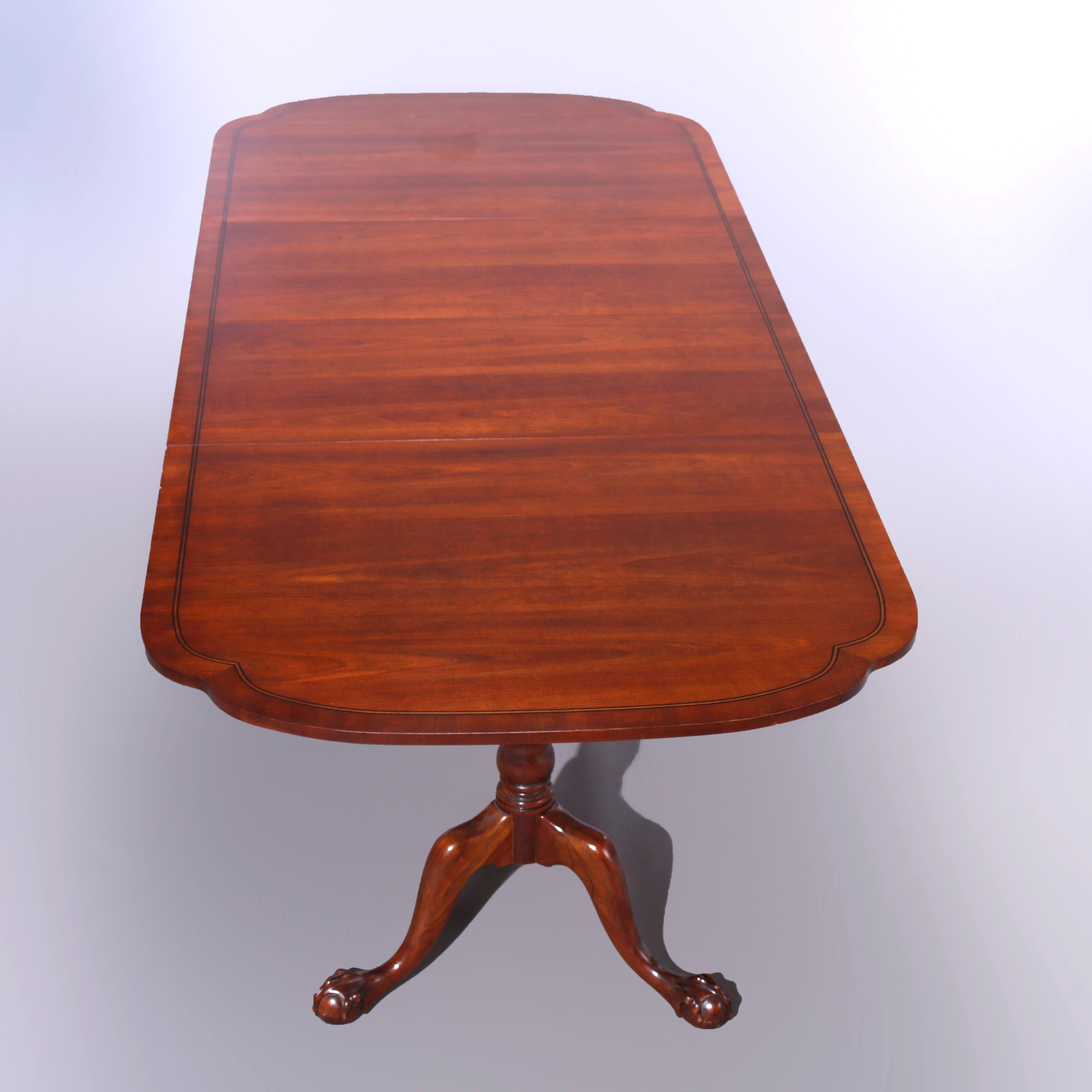An antique Chippendale style extension dining table offers mahogany construction with shaped top having inlaid ebonized banding and raised on bases with turned columns, each with three cabriole legs terminating in carved claw and ball feet, expands