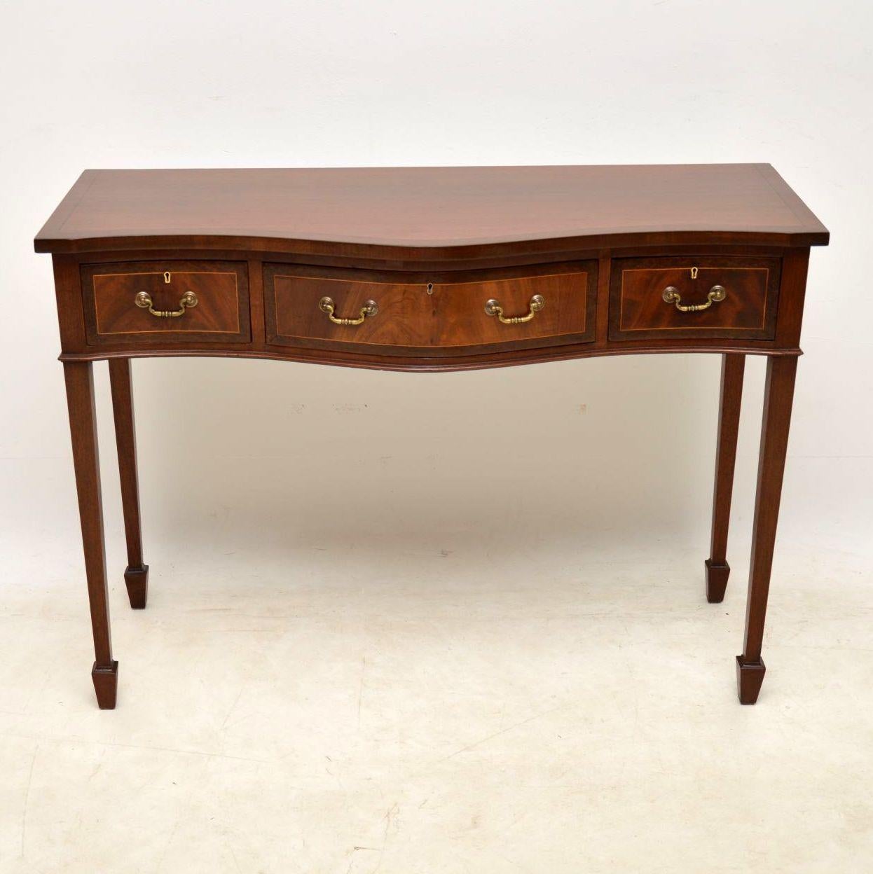 Antique mahogany console side table with a serpentine shaped front, three drawers & sitting on tapered spade end legs. The top has an ebony inlay with cross banding outside of that. The drawer fronts have flame mahogany panels with satinwood inlay &