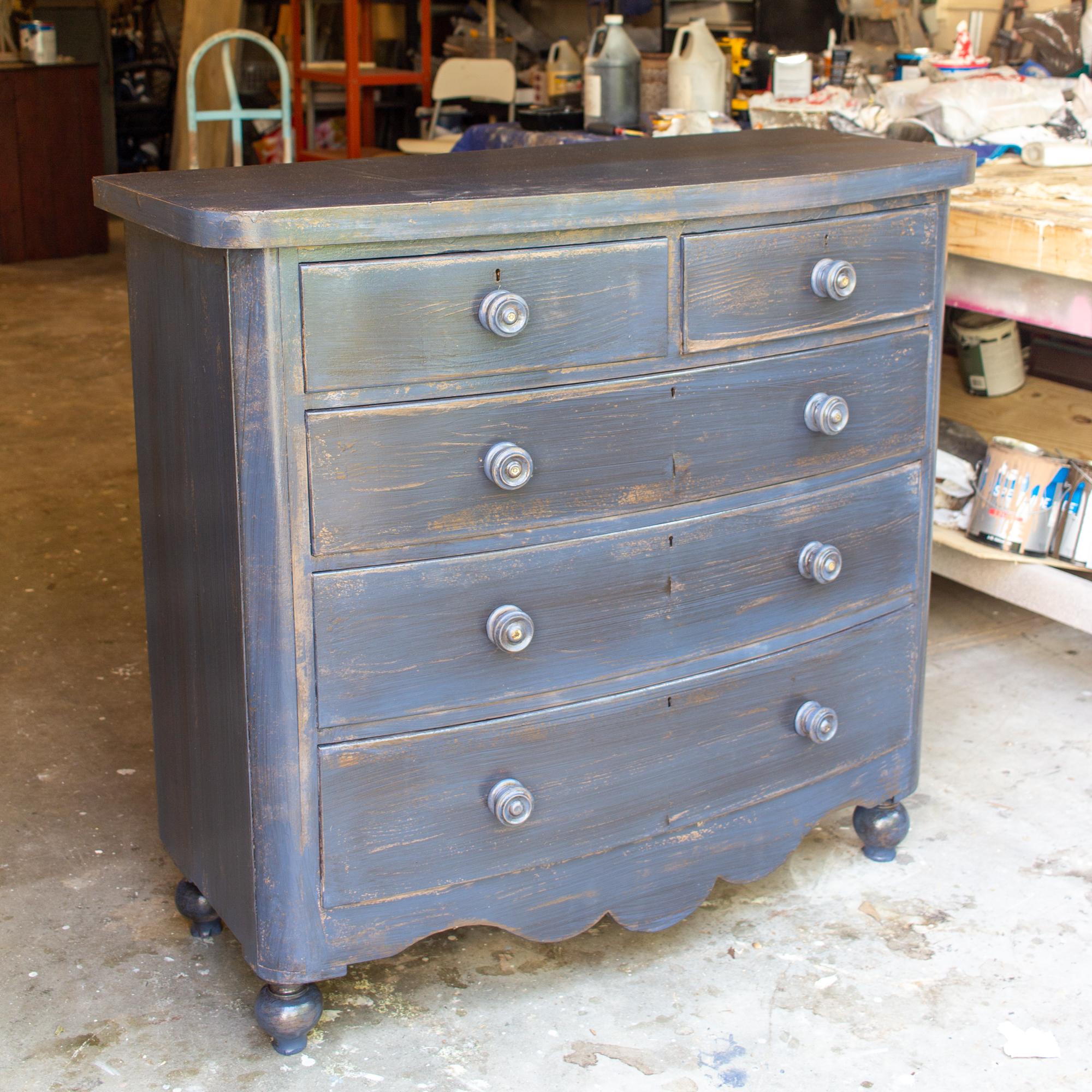This is an antique English mahogany chest of drawers with five drawers, each featuring turned handles with mother of pearl inlay on the front of each pull. Decorative feet add an additional element to this otherwise simple, curved-front dresser. The