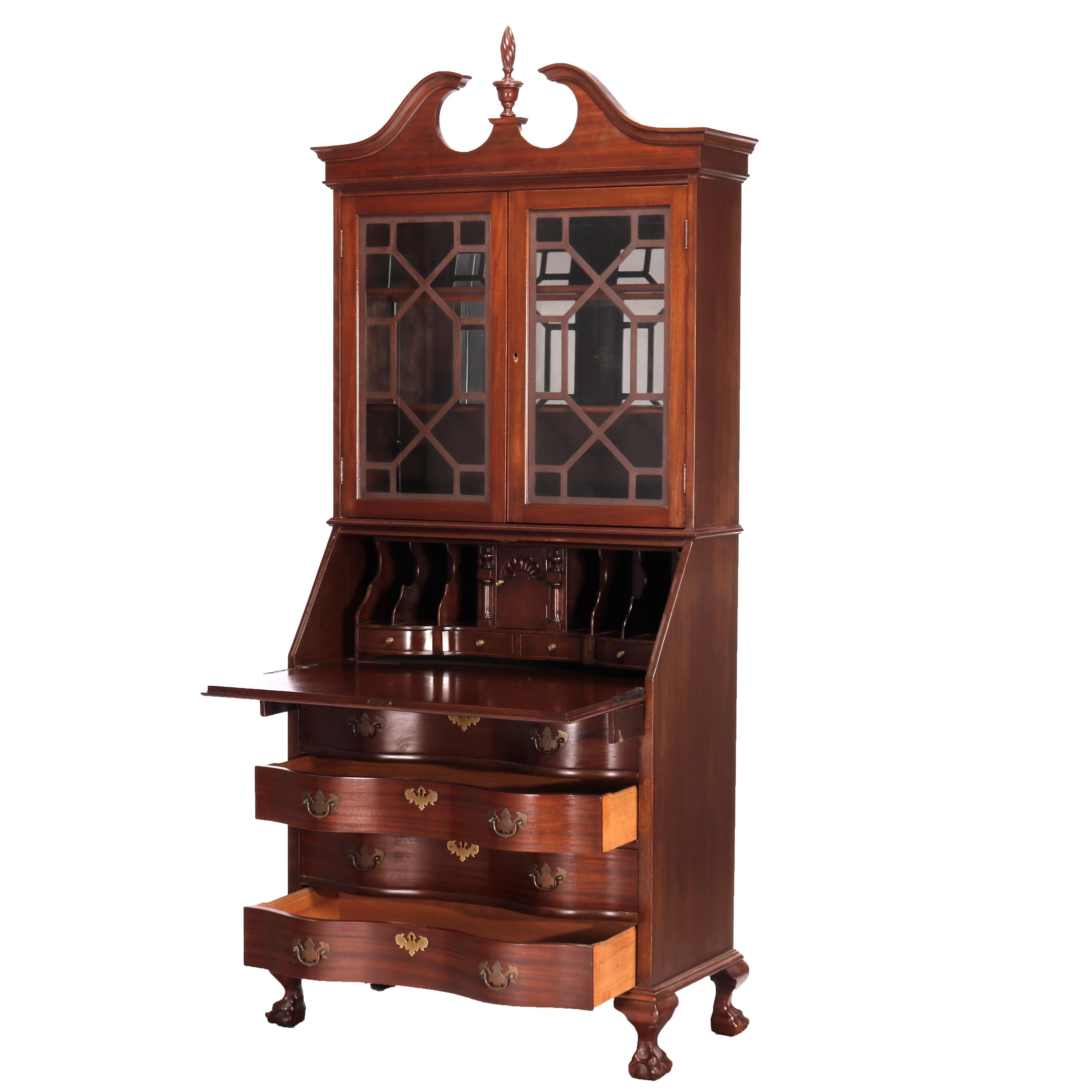 An antique Governor Winthrop secretary offers mahogany construction with upper having broken arch crest with central flame finial over double door bookcase, seated on lower with drop down desk over serpentine case with four drawers and raised on