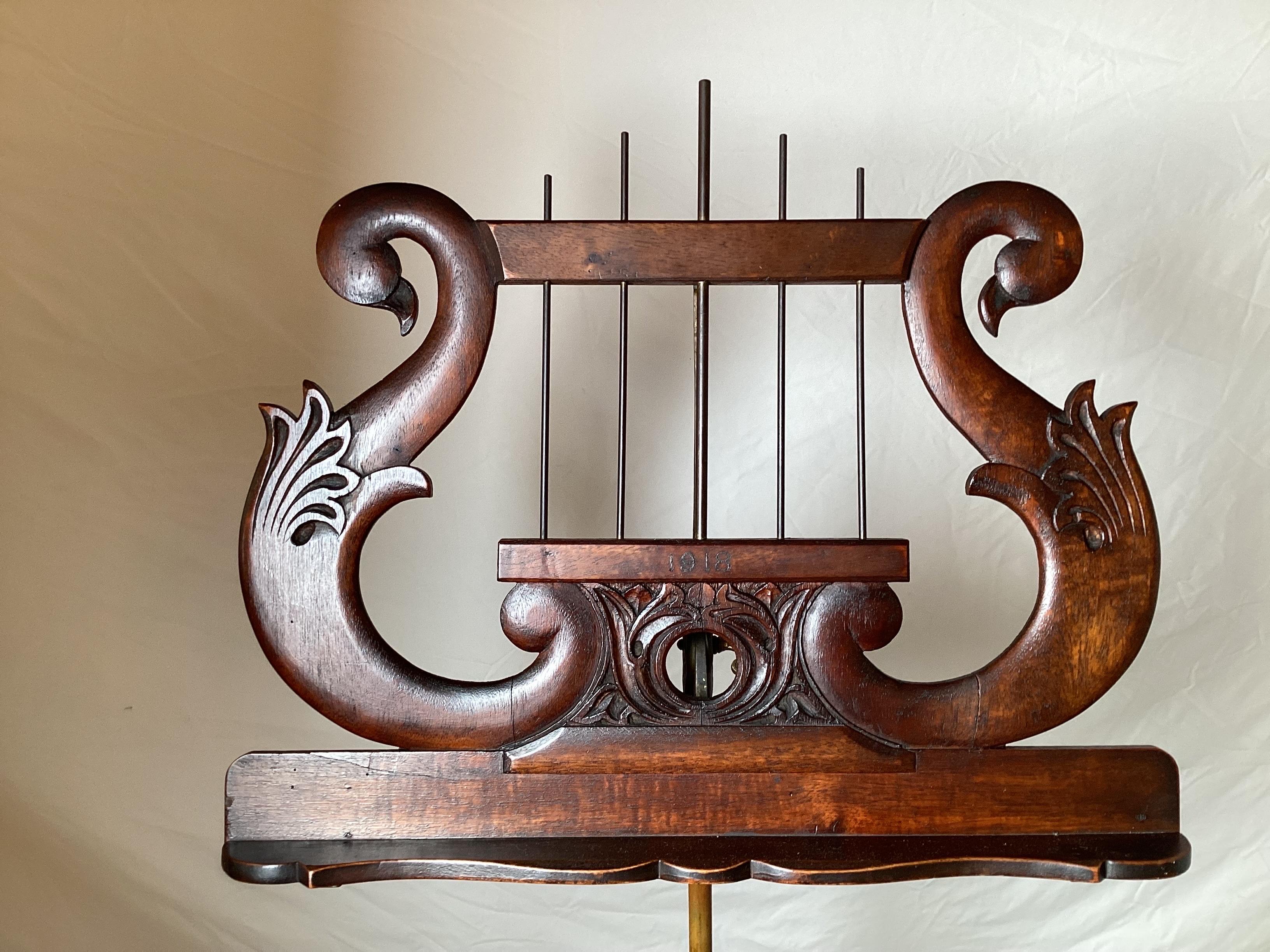 A hand carved mahogany pedestal base adjustable music stand. The base with rabbit carvings with winged cupids the can be removed from in between the three legs. The top tils and the stand adjusts from 46 to 54 inches. Marked Palmer, NY on the ring