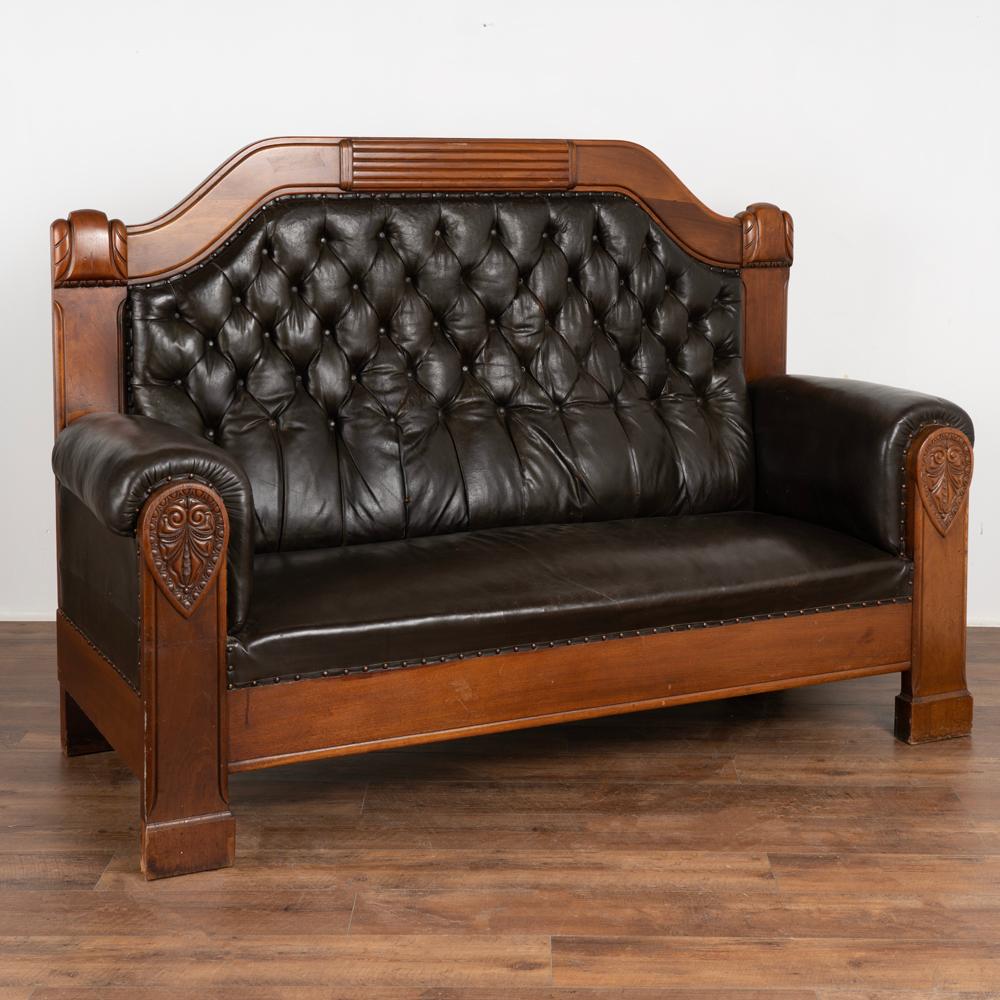 Handsome mahogany high back sofa made more impressive with carved decorative accents and heavily rolled armrests.
The dramatic high back is upholstered in dark brown vintage leather. Classic tufted style with deep padding and self covered buttons