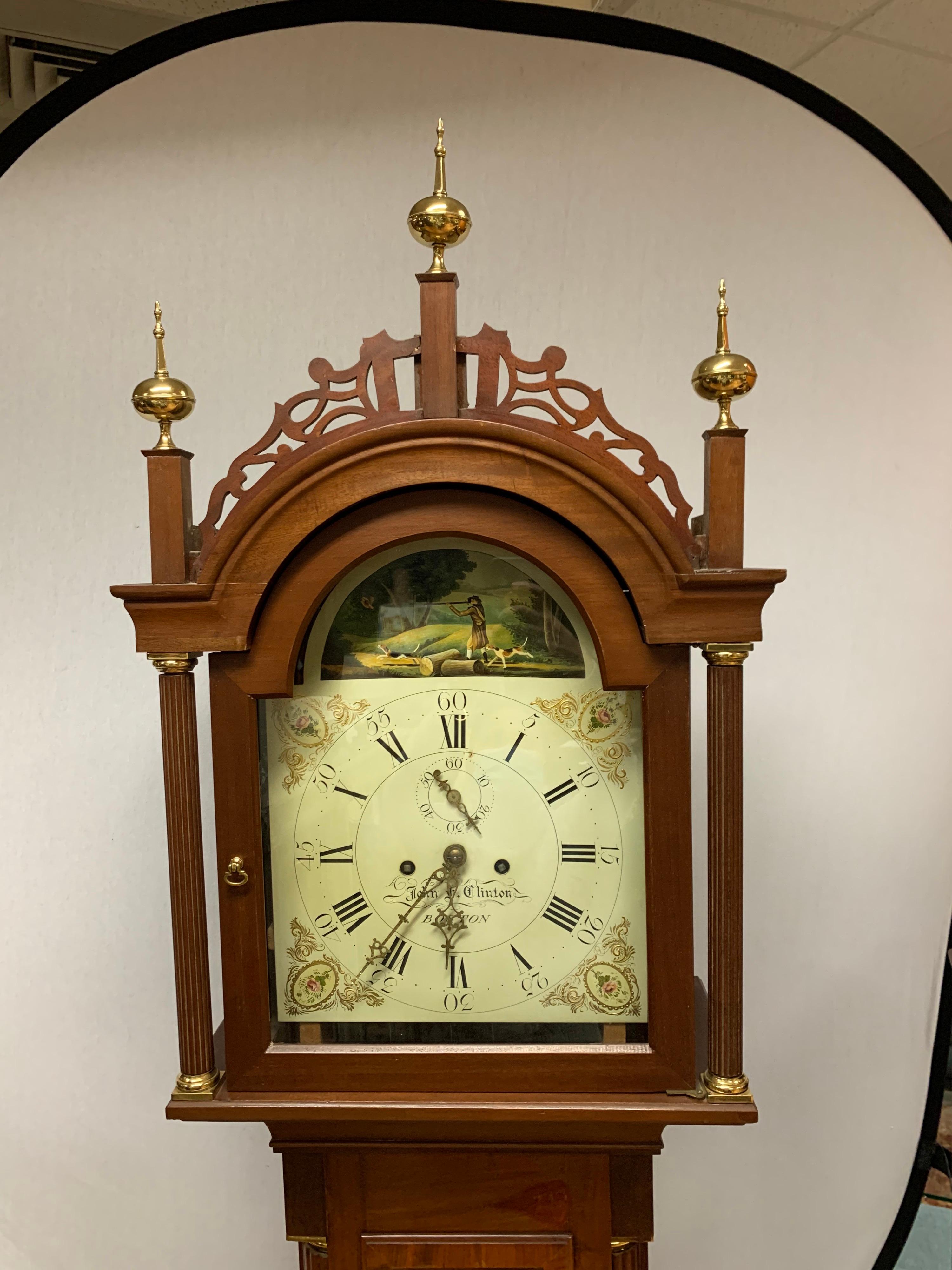 An antique George III style longcase clock, with fine mahogany veneers and craftsmanship by cabinet maker John F. Clinton in 1910. The hood is flanked with fluted columns with brass caps and base. The clock face was recently hand painted and depicts