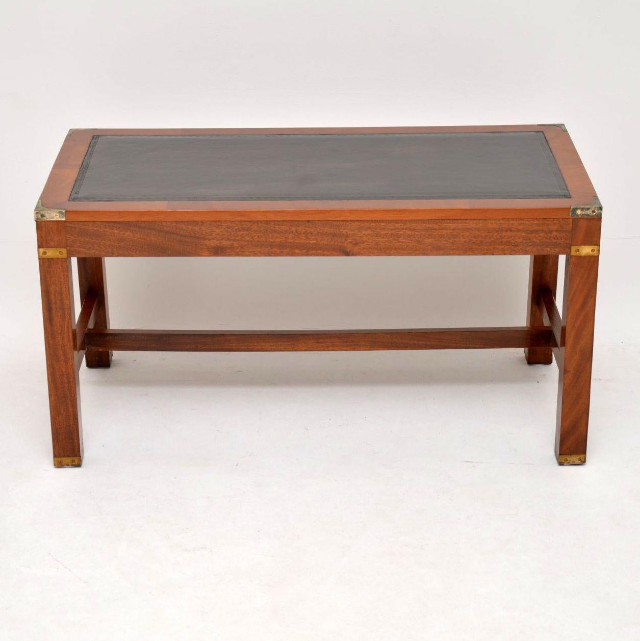 This chunky mahogany leather top coffee table is antique military style with brass corner fittings and brass capped feet. The leather top has a tooled edge and there are cross stretchers between the legs. This is a strong looking well made piece and