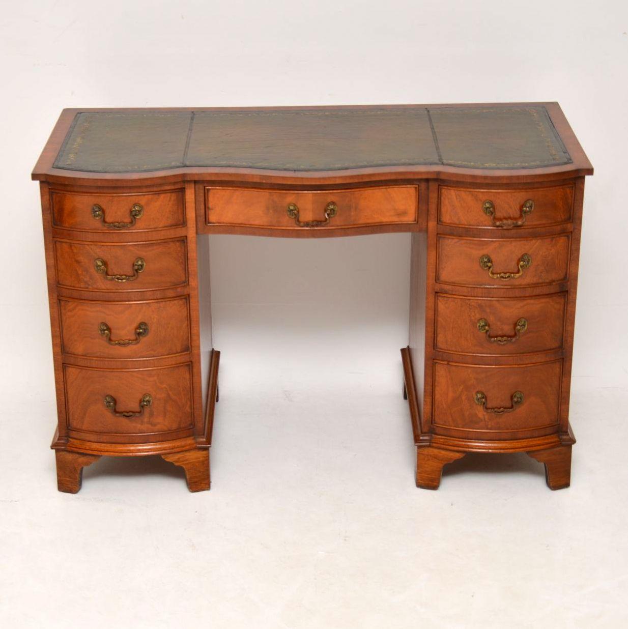 Antique Regency style flame mahogany pedestal desk with a tooled leather writing surface and in excellent condition. It has a double serpentine shaped front and drawers of graduated depth with beautifully cast brass handles. This desk sits on