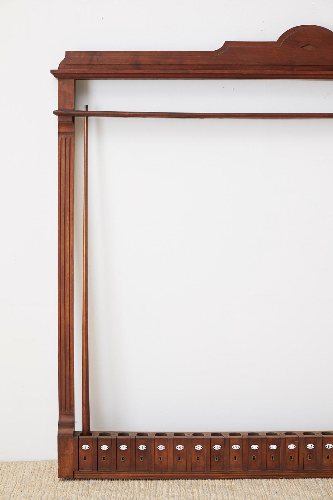 Large antique billiards, snooker, or pool cue rack constructed from mahogany. Features 24 small locking doors labeled with white enamel numbers. There are 10 original skeleton keys that are numbered included with the rack. The frame of the rack has