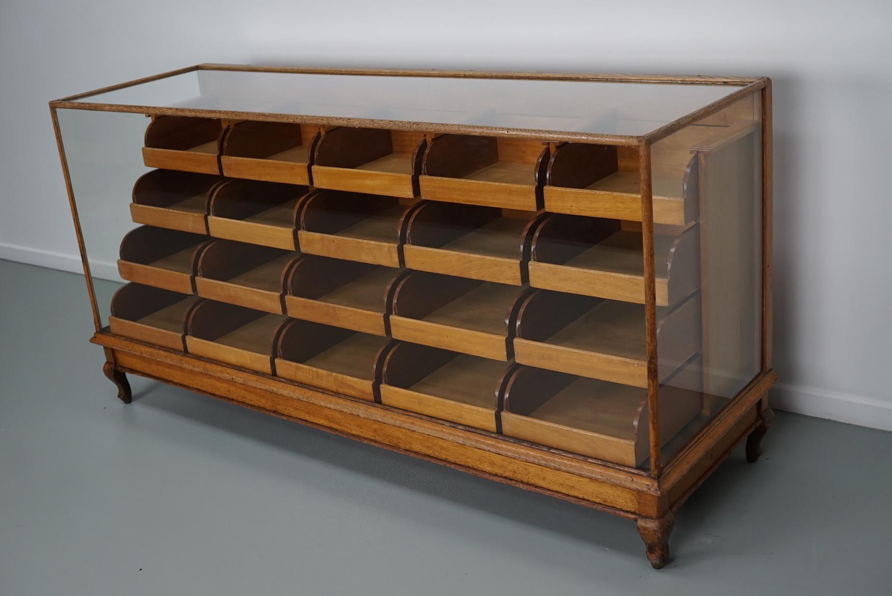Dieser Kurzwarenladentisch aus Eiche stammt aus dem späten 19. Jahrhundert und wurde in England hergestellt. Er besteht aus einem massiven Holzrahmen, einem Glasgehäuse und 20 Schubladen aus Mahagoni mit Messinggriffen.