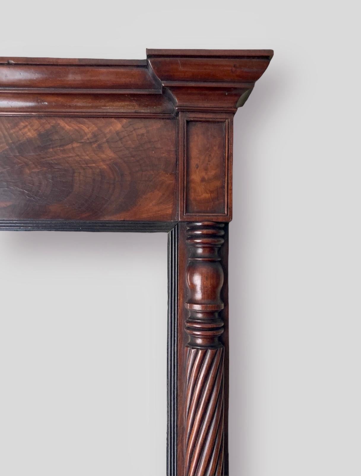 Antique Mahogany Overmantle Pier Mirror featuring a molded cornice, flame frieze and reeded molding. The mirror plate is flanked by slim twisted columns on either side.