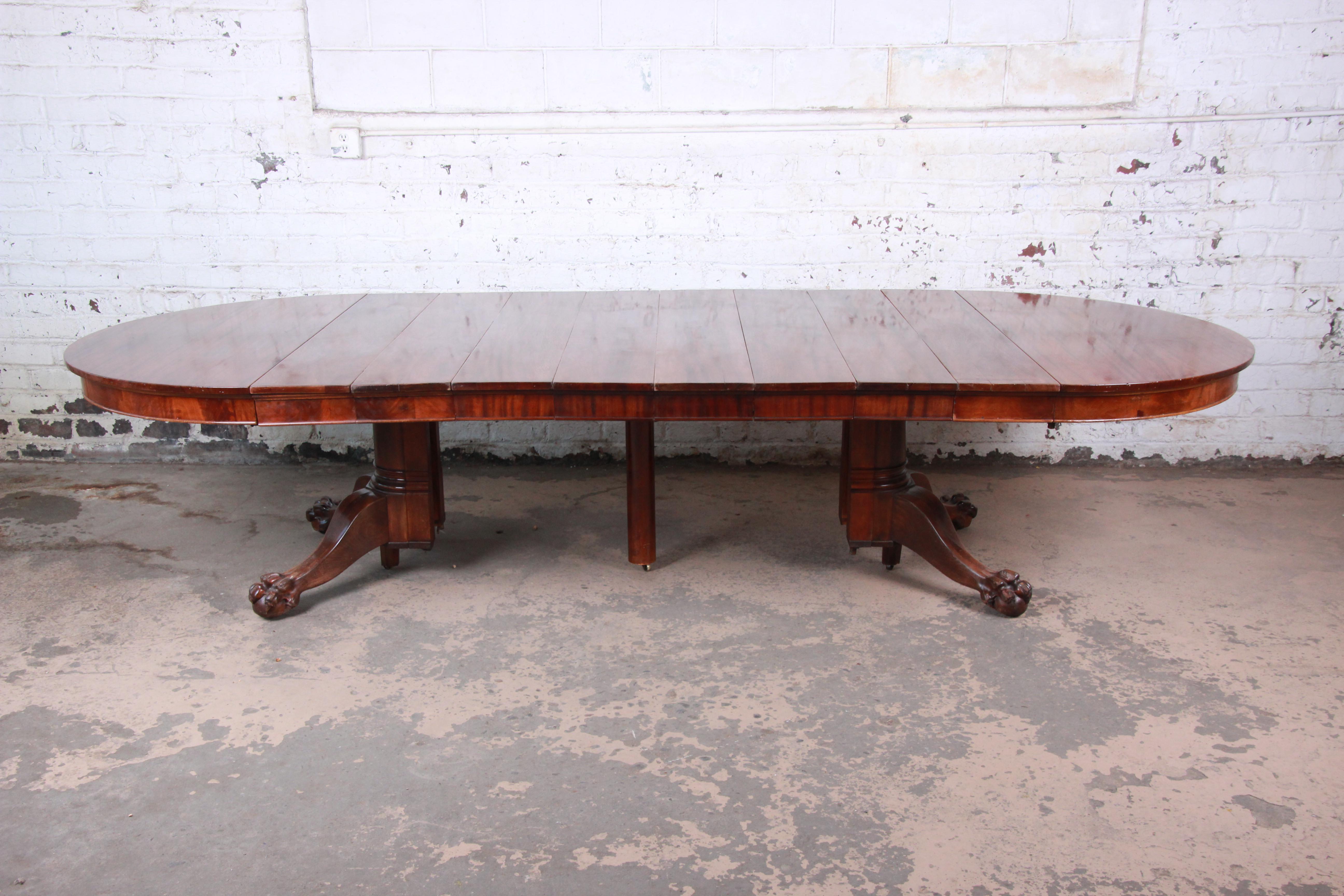 An outstanding antique mahogany extension dining table with carved paw feet. The table features gorgeous flame mahogany wood grain and a nice carved pedestal. It measures 54.5