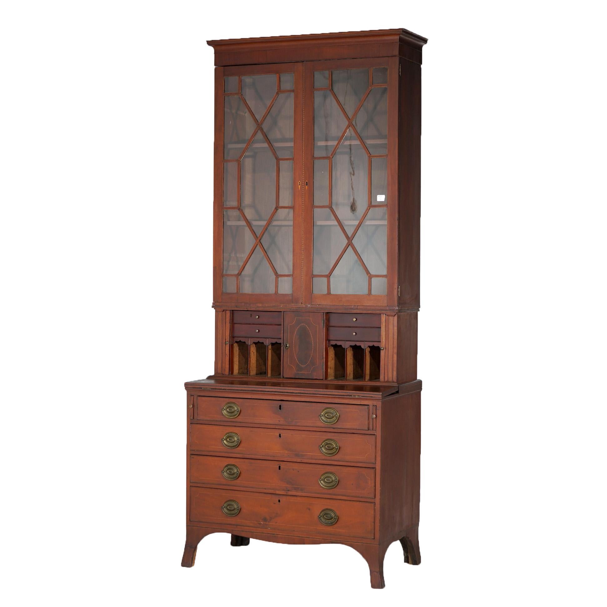 An antique secretary offers mahogany construction with upper bookcase having double mullioned glass doors surmounting desk with tambour doors opening to storage compartments and drop-down writing surface over lower case having graduated long drawers