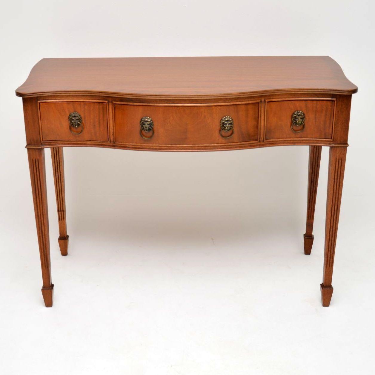 Antique mahogany server, side or console table in good condition and dating from circa 1930s-1950s period. It has a serpentine shaped front, with a reeded top edge, reeded legs and spade end feet. There are three drawers with brass lion head handles