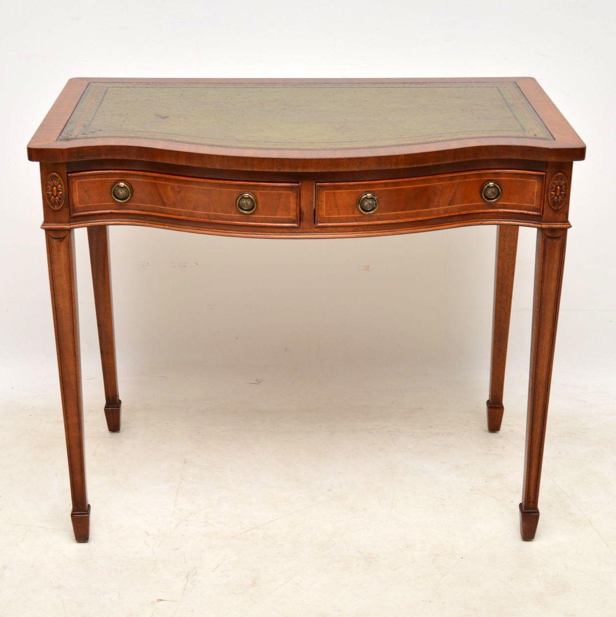 Antique Sheraton style leather top writing table in good condition dating from the 1950s period. It has a nice character original tooled leather writing surface. The front is serpentine shaped and there are two drawers with inlay, cross banding and