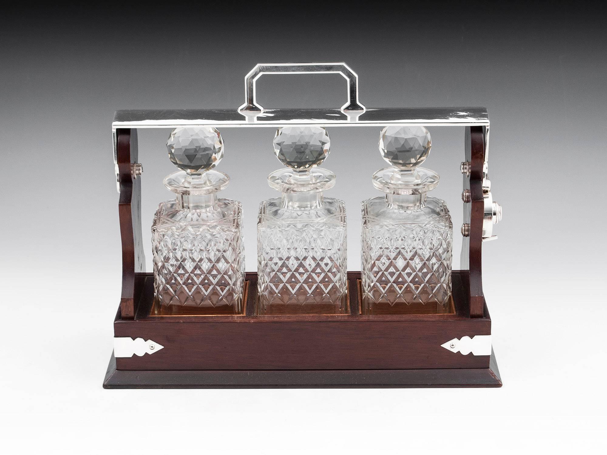 Antique Mahogany Tantalus with silver plate handle and corner brackets. 

The silver-plated brass handle is marked: 
142 & 144 JAYS Oxford St. W 

Contains three hobnail cut crystal decanters with faceted stoppers. Once unlocked the key barrel