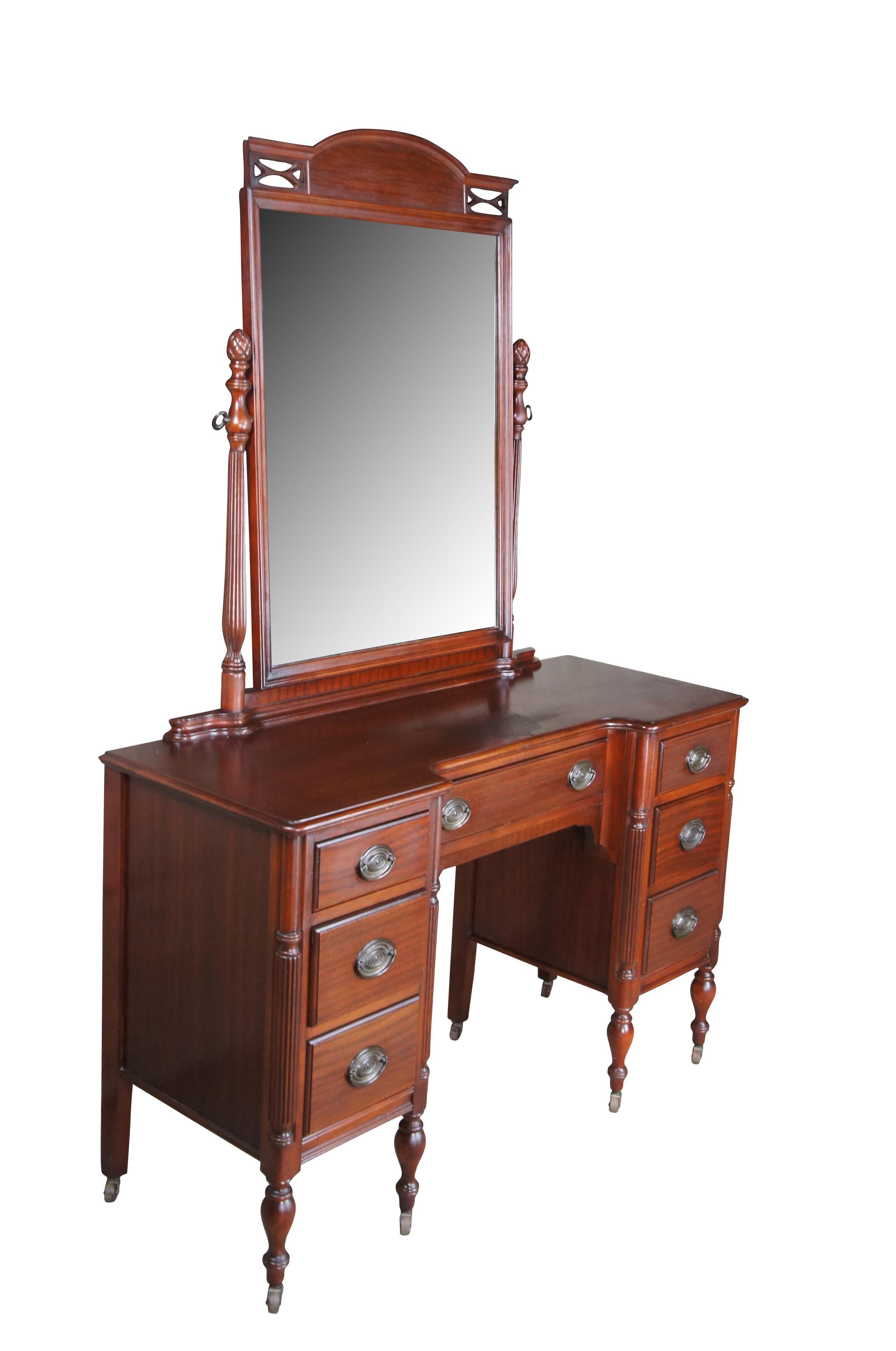 Antique vanity desk or dressing table.  Made of mahogany featuring rectangular form with seven drawers over eight turned legs with swivel castors, and upper mirror with reticulated crown flanked by fluted pineapple posts.


DIMENSIONS

48
