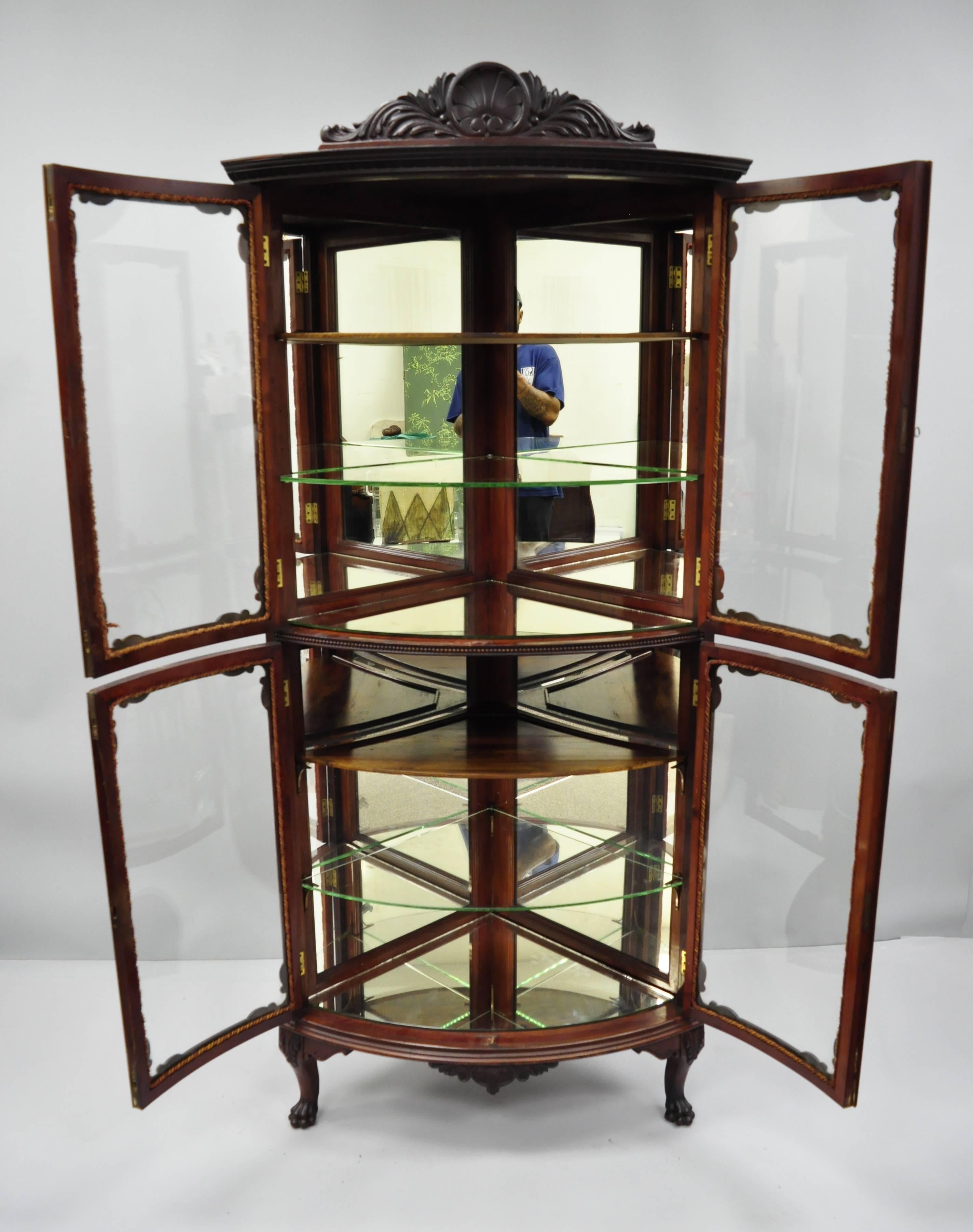Antique mahogany Victorian bow glass corner curio cabinet. Item feature a shell carved pediment, four bow glass doors, carved paw feet, two wooden shelves, two clear glass shelves, two mirrored shelves, finely carved details, working lock and key,