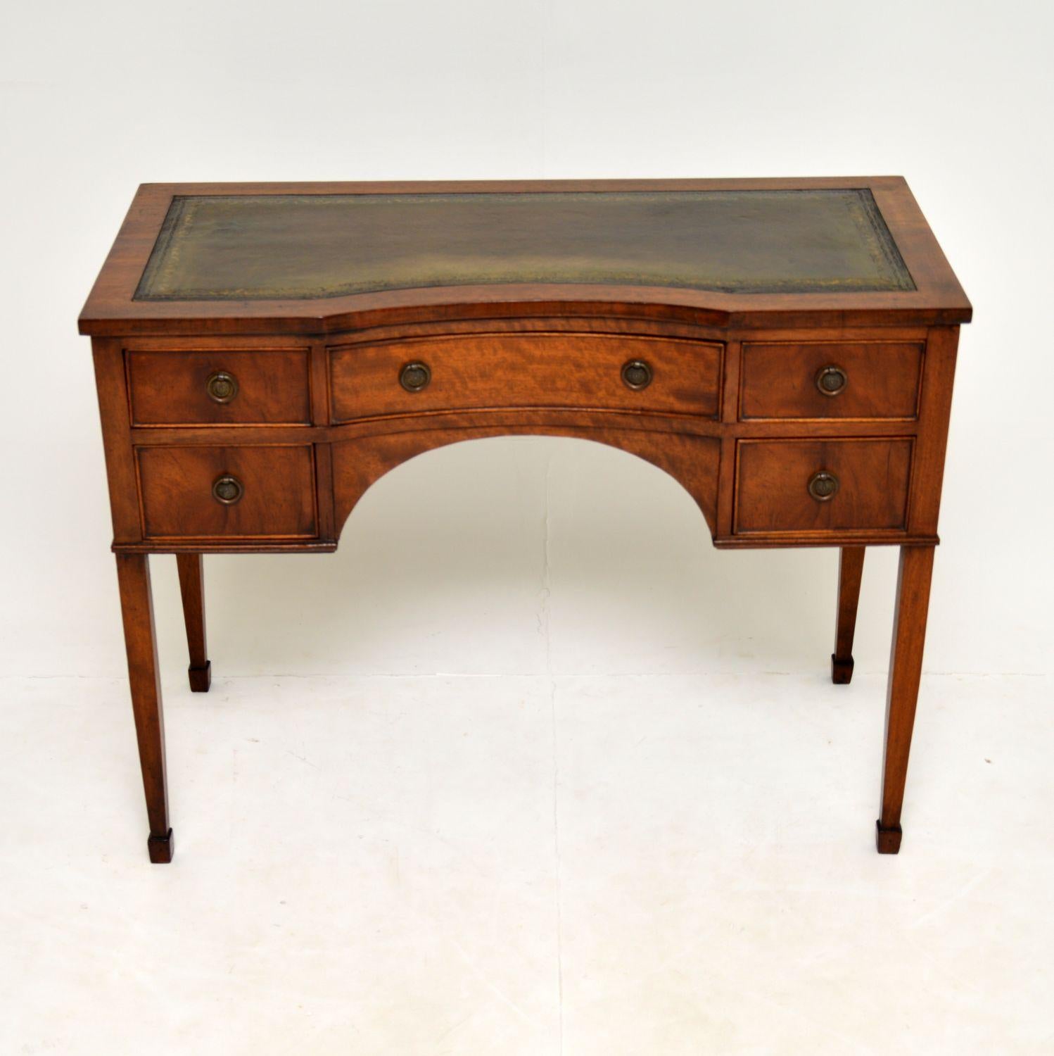 A lovely antique writing table in mahogany, with an inset leather top. This dates from around the 1900-1910 period & is antique Sheraton style.

It is of superb quality, and is beautifully made from mahogany. This has an inverted serpentine front,