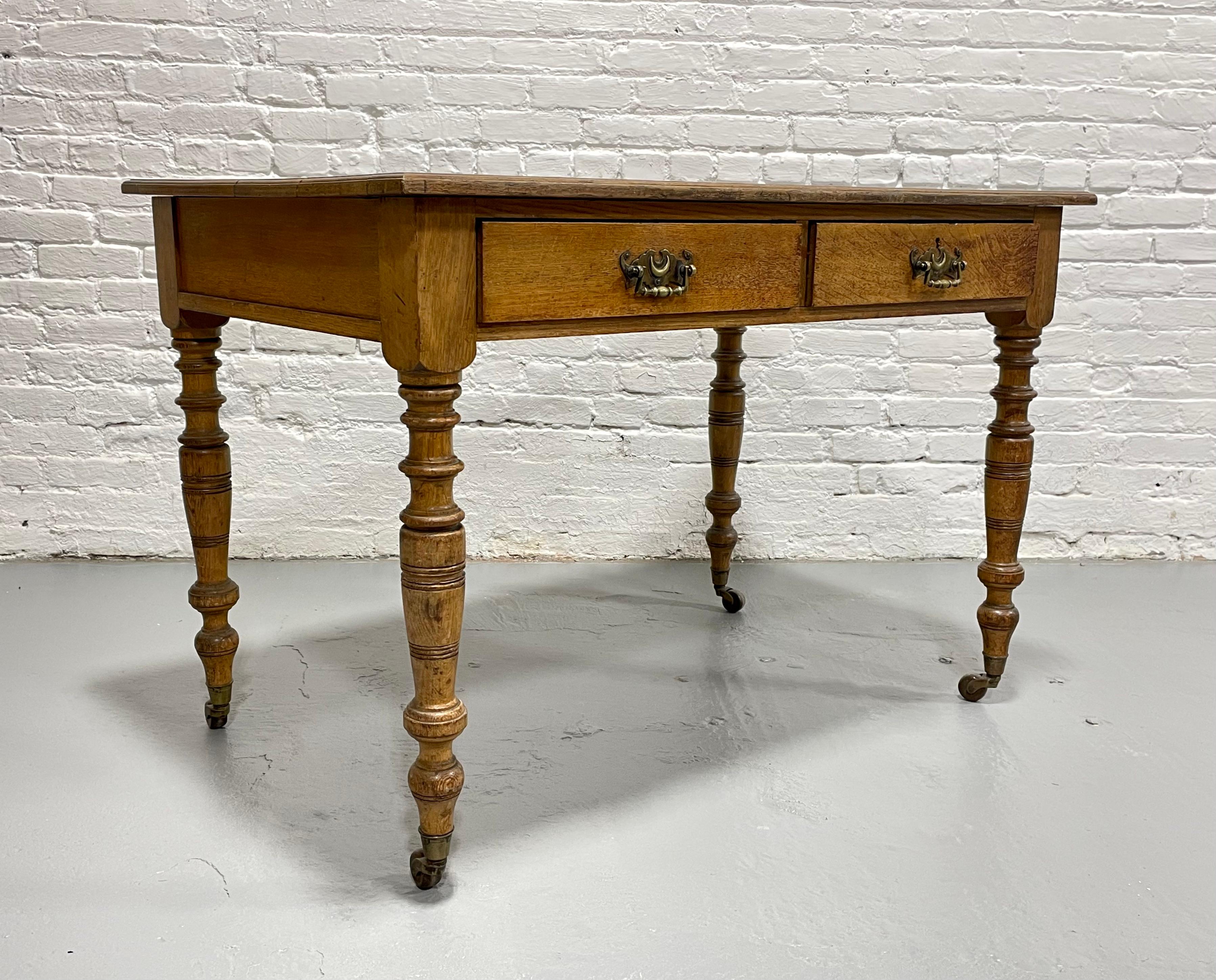 Handsome Antique Writing Table or Server featuring turned legs on castors, c. 1890. Two drawers with lovely pulls, a gilt embossed red leather top and interesting period casters. Perfect little writing desk that can easily roll to change positions