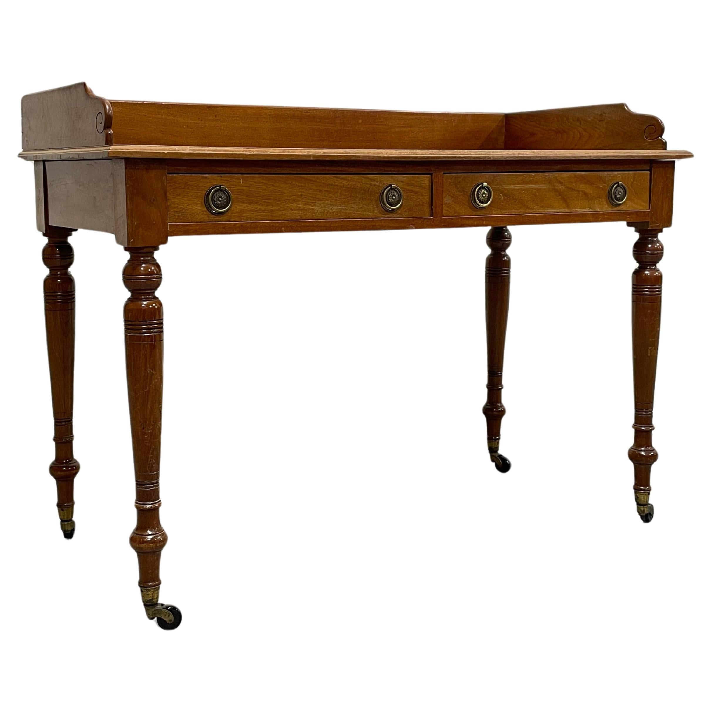Handsome Antique Writing Table or Server featuring turned legs on castors, c. 1890. Two drawers with lovely pulls, a gilt embossed leather top and interesting period casters. Perfect little writing desk that can easily roll to change positions if