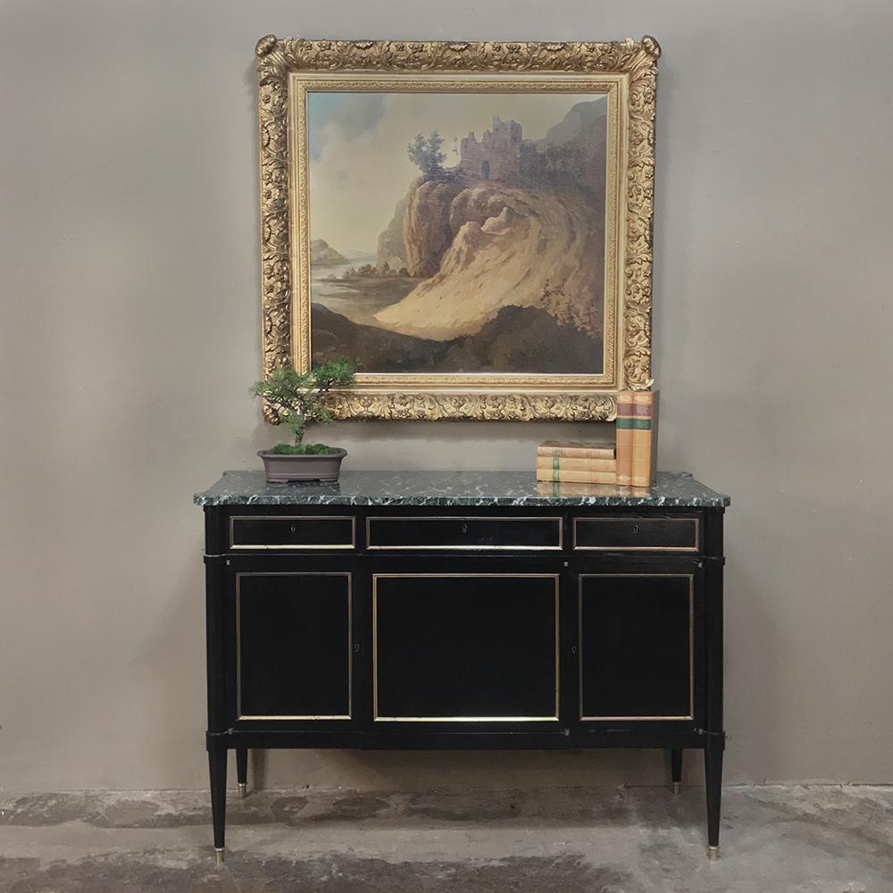 Antique Maison Jansen style Louis XVI marble-top buffet features the tailored lines for which the style became famous. A beautifully veined marble top appears above the ebonized panels below, which are framed in gold highlighting. Tapered legs with