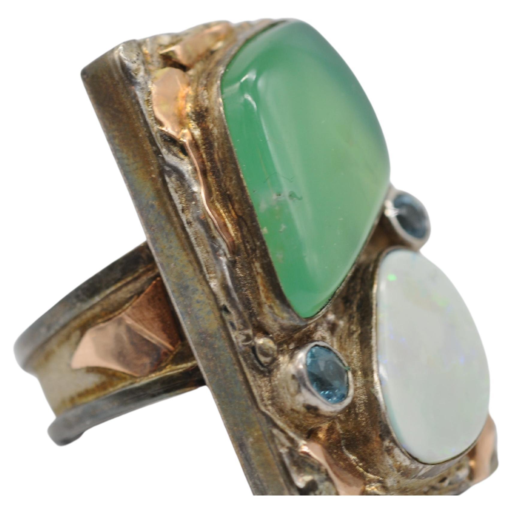 Entrez dans un monde d'élégance intemporelle avec cette exquise bague en argent ancien, ornée de délicats accents d'or rose et d'une étonnante gamme de pierres précieuses, dont l'opale, l'aigue-marine et peut-être le jade. Cette bague captivante