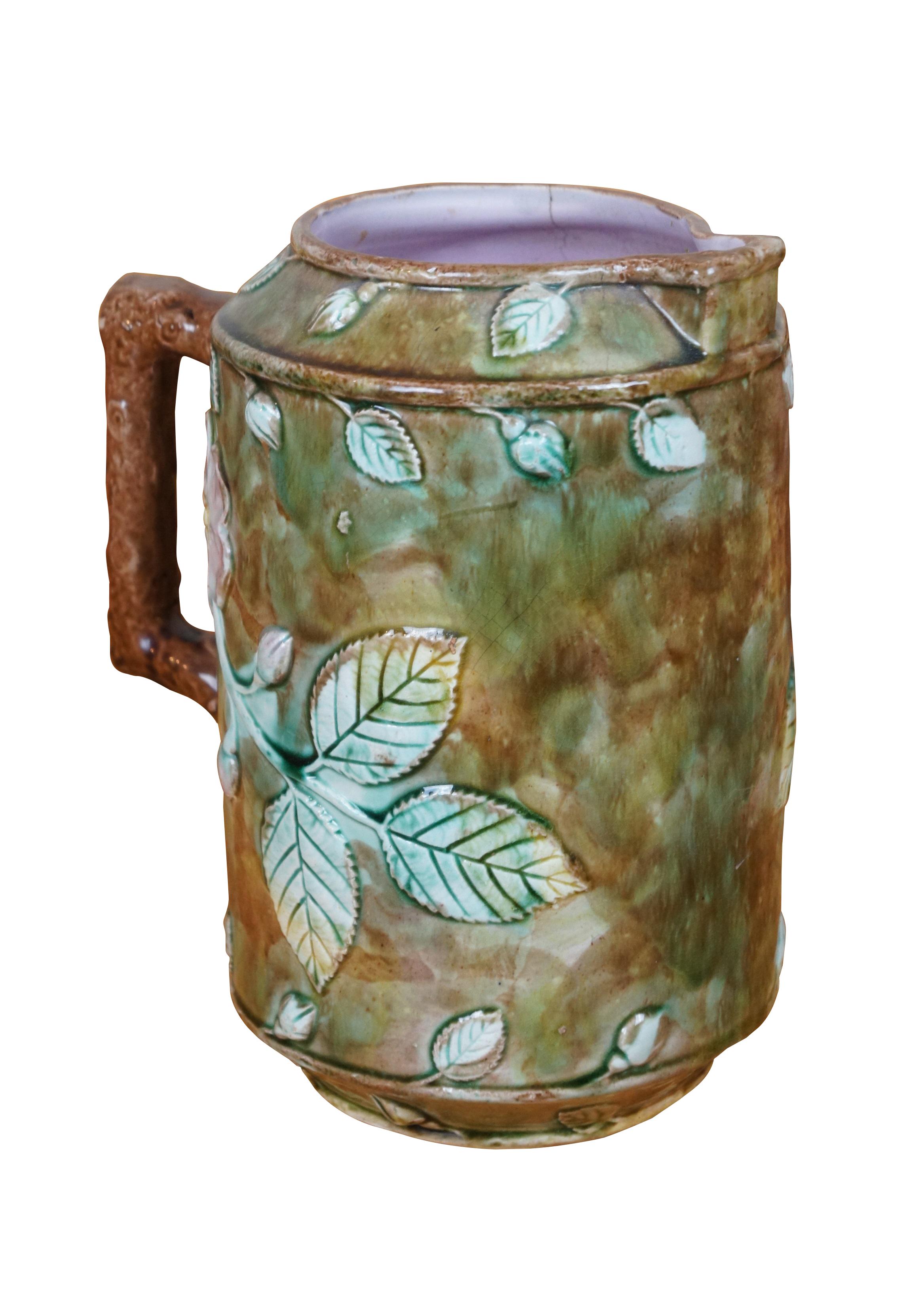 Very large antique Majolica French Barbotine pitcher / jug / carafe featuring a green and brown field with wild dog rose flower blossoms and a twig / branch handle, and purple lavender interior.

Dimensions:
8.25