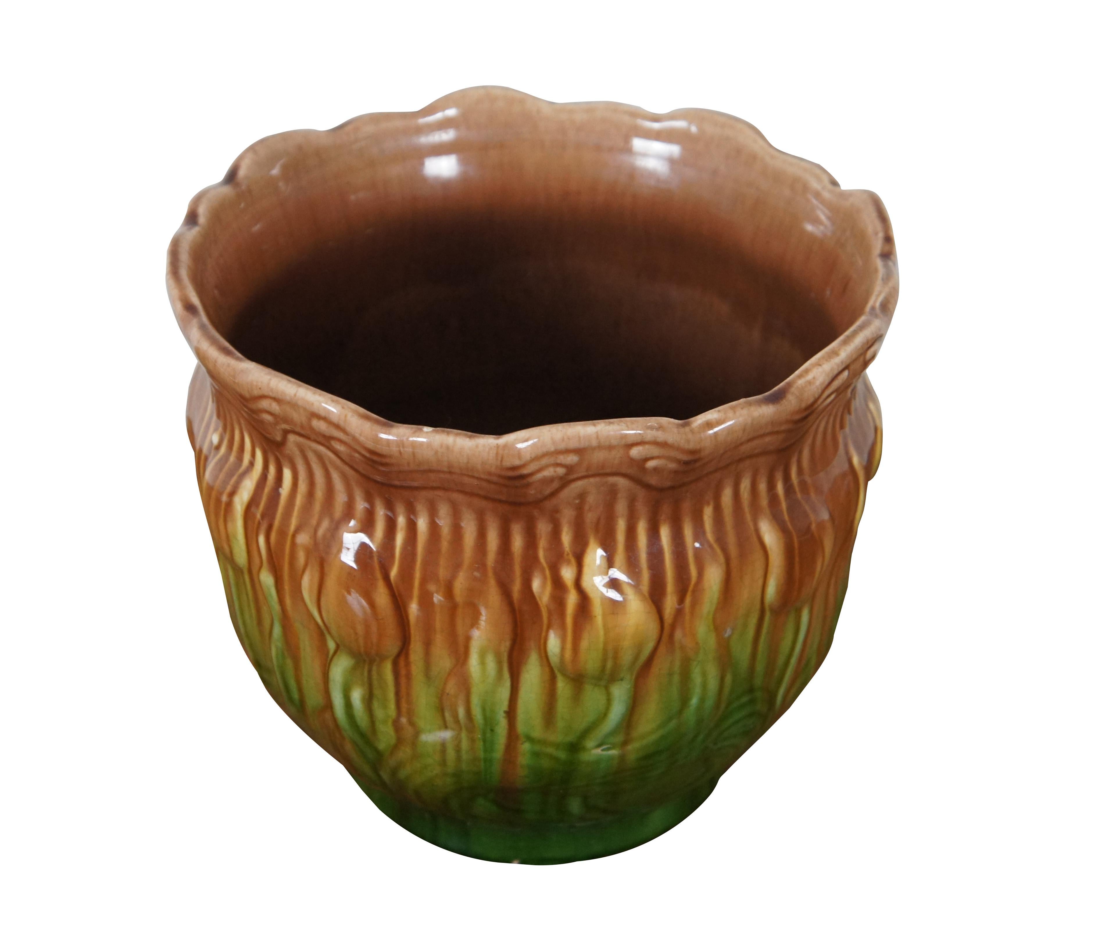 Antique majolica pottery planter / jardiniere with a round form, footed base and flared, scalloped edge. Decorated with tulips in green and brown under a high gloss finish.

Dimensions:
10.5” x 8.75” (Diameter x Height)