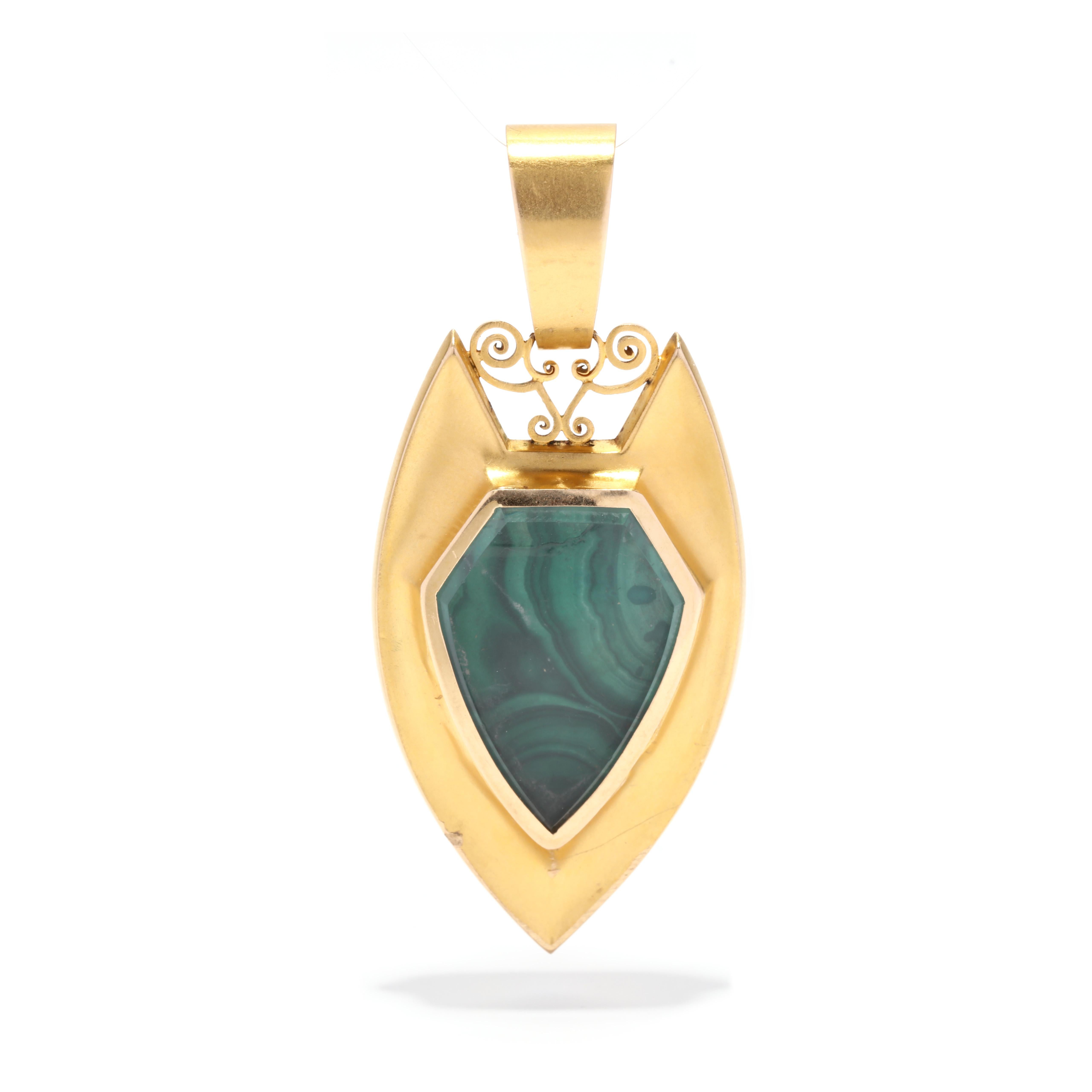 An antique malachite shield locket pendant. This Etruscan revival pendant features a pointed shield motif set with a shield cut natural malachite center stone surrounded by raised gold scroll detailing, a glass locket on the reverse and with a large