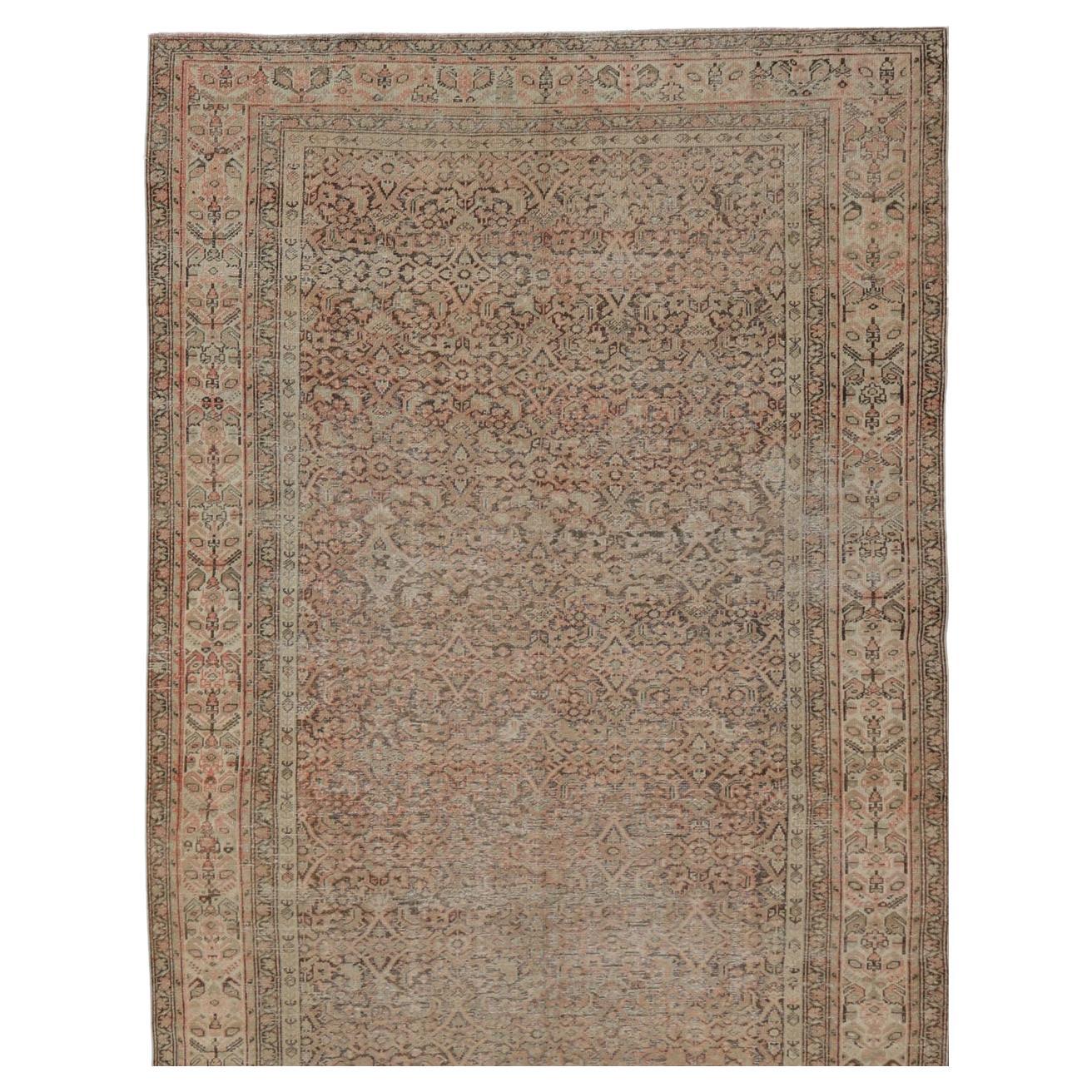 This antique Malayer rug features a modest, multi-tiered border and delicate field, busy with an all-over symmetrical design. This piece sets a quiet coffee background behind muted shades of salmon, tan, and taupe. Earthy olive undertones can be