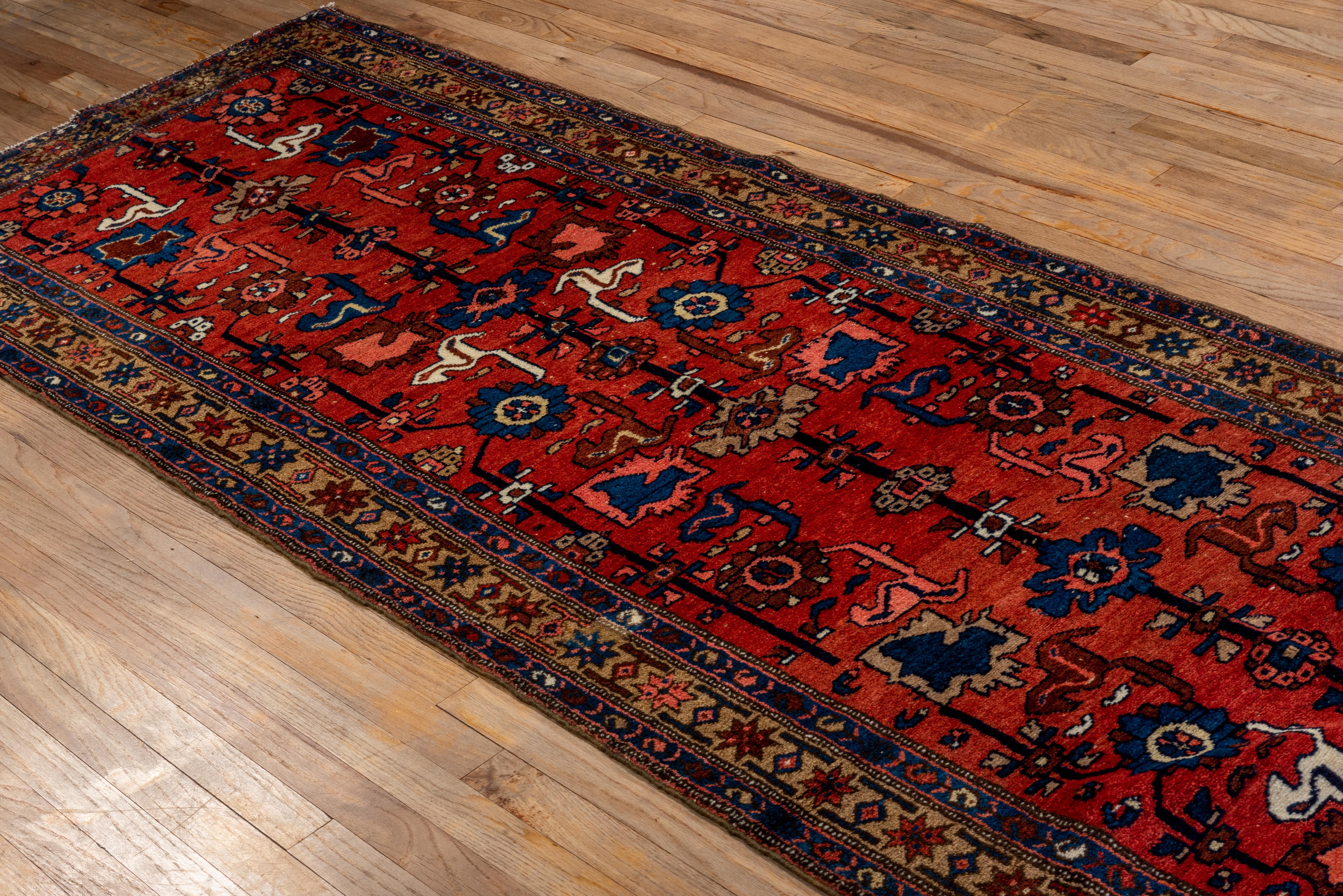 This antique Malayer runner features a rich crimson red field adorned with stylized floral rosettes, abstract animals, and geometric vinework. The palette—anchored by deep indigo, ivory, and soft camel—delivers striking contrast and rhythmic