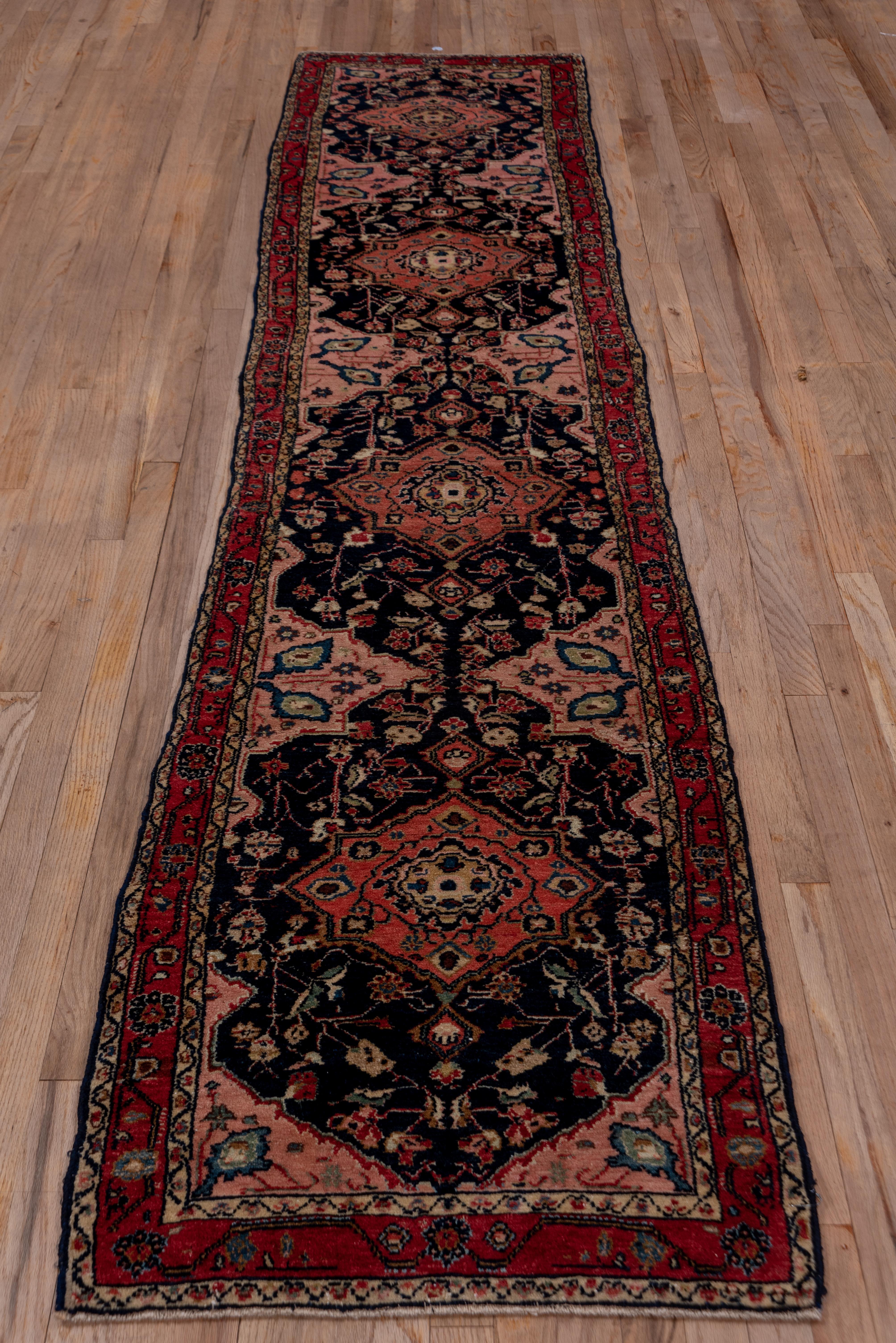 The navy field of this very good condition west Persian village runner features rose octogram medallions, flowering tendrils and fractional side fillers. The red border displays a rosette and undulating geometric vine. Light and medium blue, pale