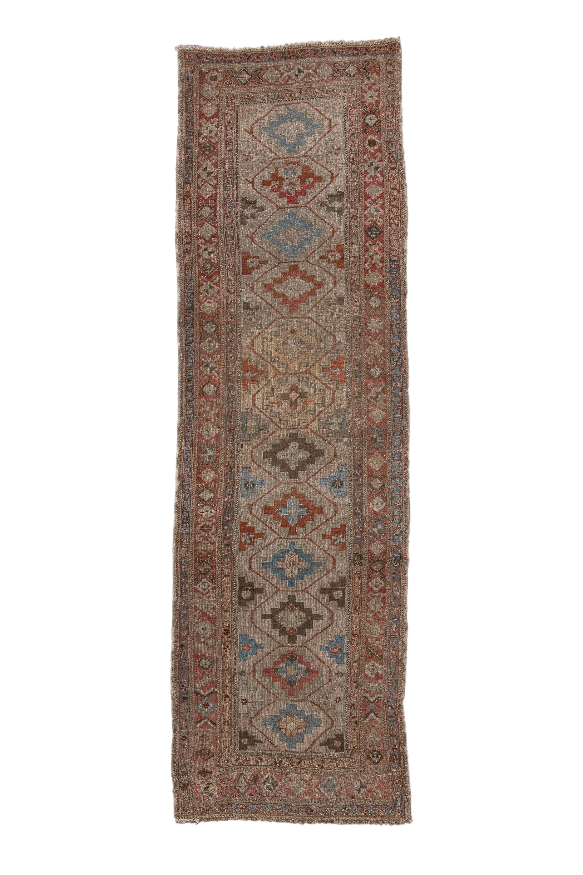 The camel-tone field shows a central column of twelve adjoined “Memling guls” enclosing stepped lozenges in red, rust, teal and beige, with half en suite lozenges along the sides. Narrow main border is in the Turkmen style with rams’ horn