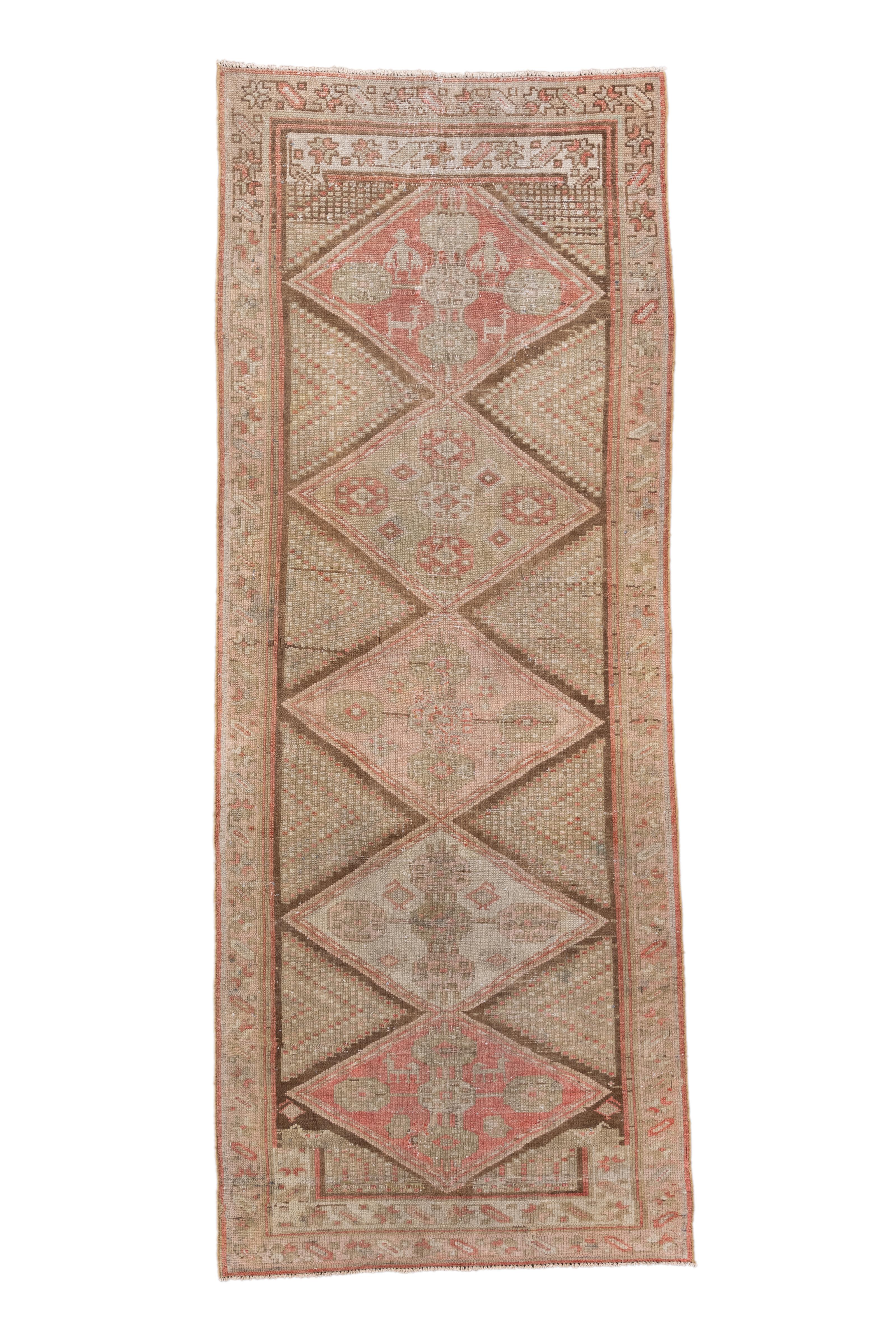 This antique Malayer runner presents a captivating diamond medallion design in a rich yet delicately faded palette of terracotta red, soft sage, pale blush, and muted taupe. The repeating geometric diamonds are filled with tribal symbols and flanked