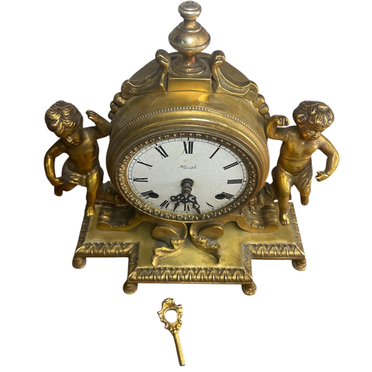 Cette horloge de cheminée fonctionnelle, entourée de deux anges, est dotée d'un cadre en bronze doré massif, fabriqué et fini à la main. Son mécanisme (mouvement huit jours) est allemand et le mouvement mécanique à remontage manuel a été fabriqué