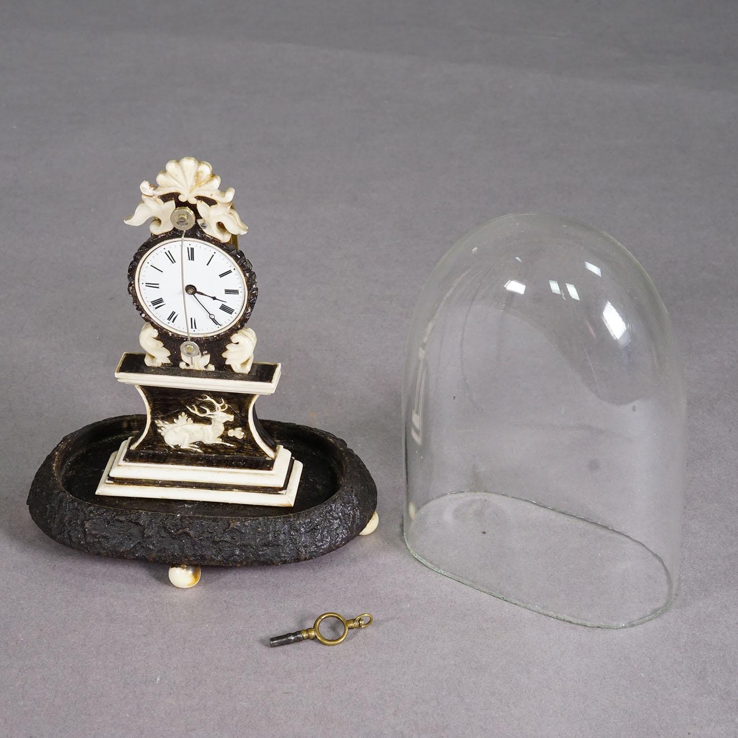 Antique Mantel Clock under Glass Dome, ca. 1870

This is a finely crafted mantel clock from around 1850–1880, housed under a rounded glass dome on a textured base resembling tree bark. The clock features a beautifully carved pedestal with a stag