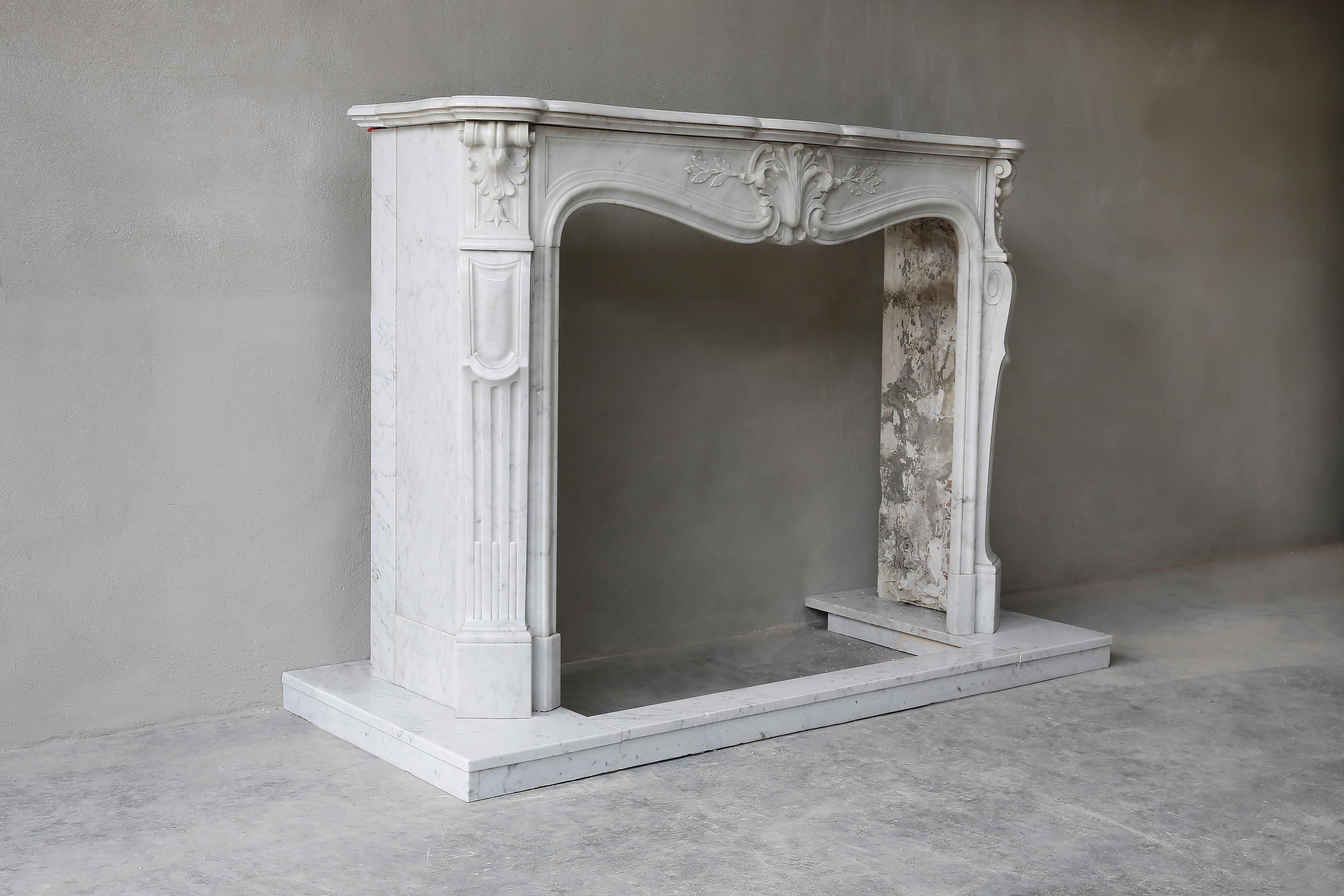 A beautiful antique fireplace in Carrara marble from the 19th century including a plateau of the same marble. This beautifully decorated chimney is in Louis XV style and features 'trois coquilles' (3 shells) and various elegant ornaments. A very