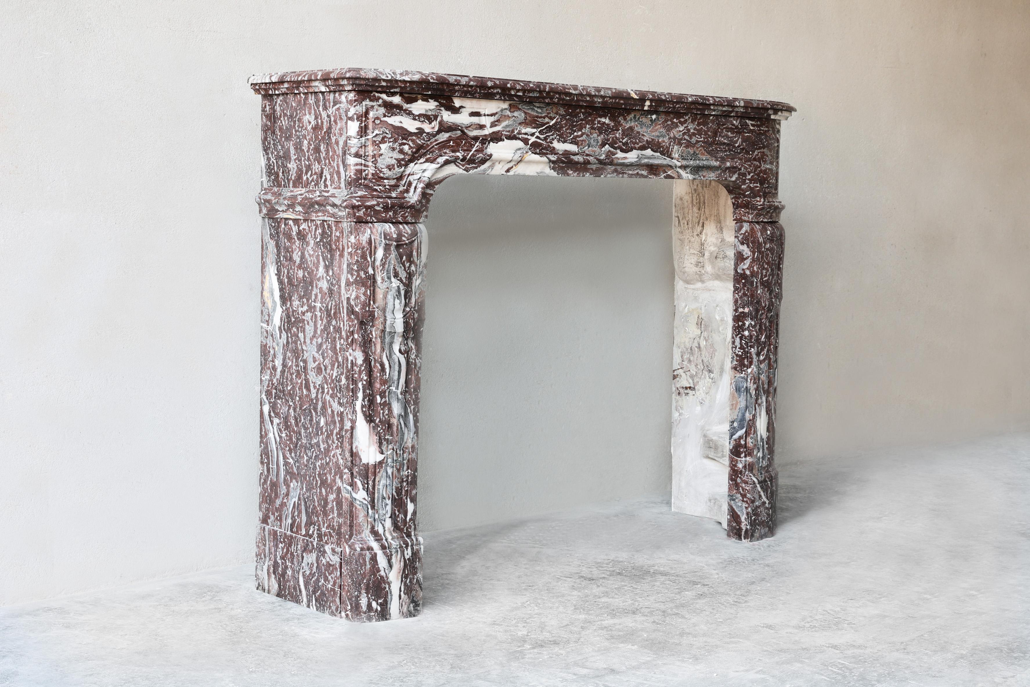 This antique fireplace is a remarkable example of 19th-century craftsmanship. It was made in Paris, France, between 1860 and 1880 and follows the elegant proportions of the Louis XIV style. The material used is Griotte de Campan Rouge, a
