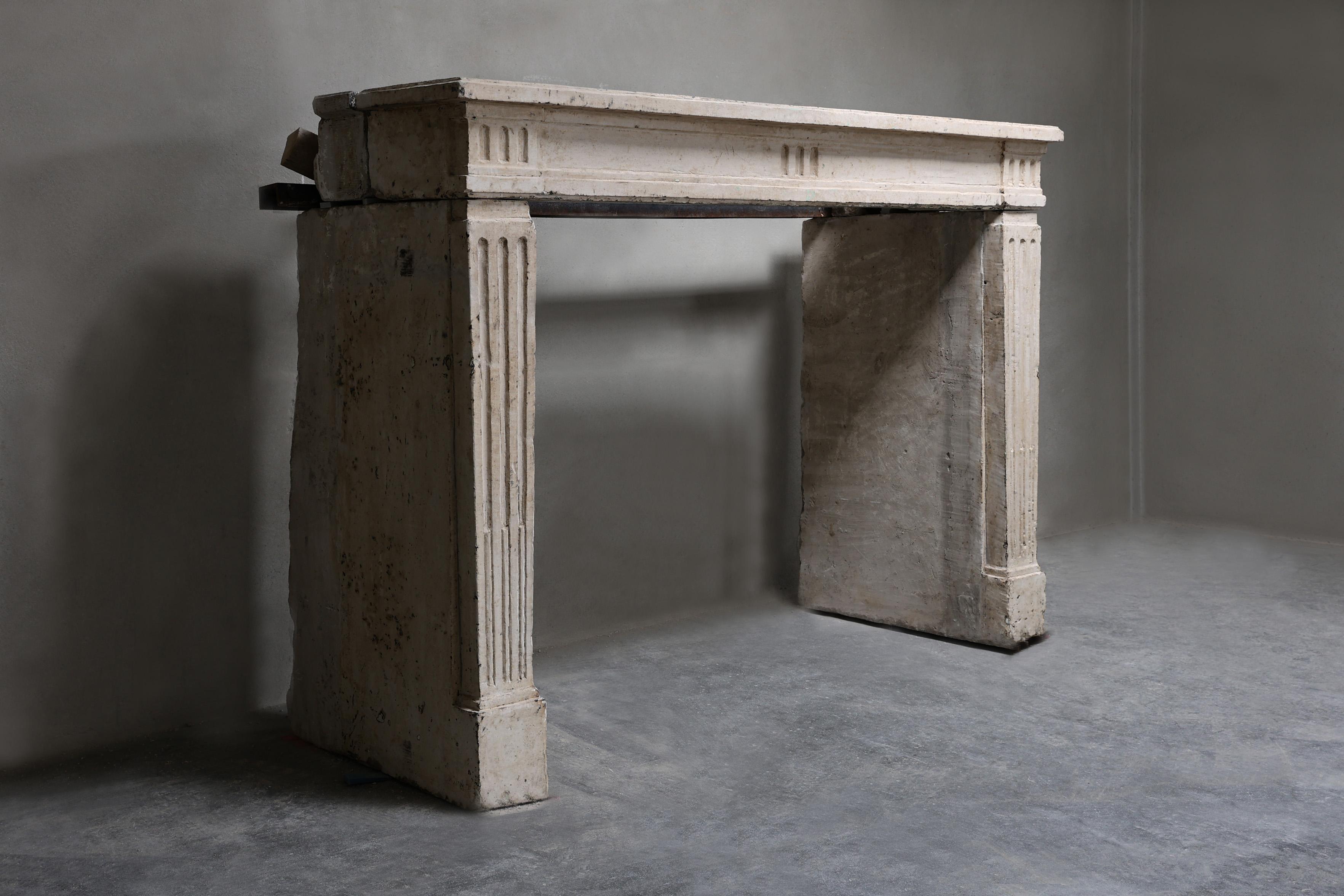 Cette cheminée ancienne du XIXe siècle est réalisée en pierre calcaire française et exécutée dans le style Louis XVI. Le design épuré et rectiligne avec de fines lignes verticales donne un aspect calme et classique. La cheminée allie simplicité et