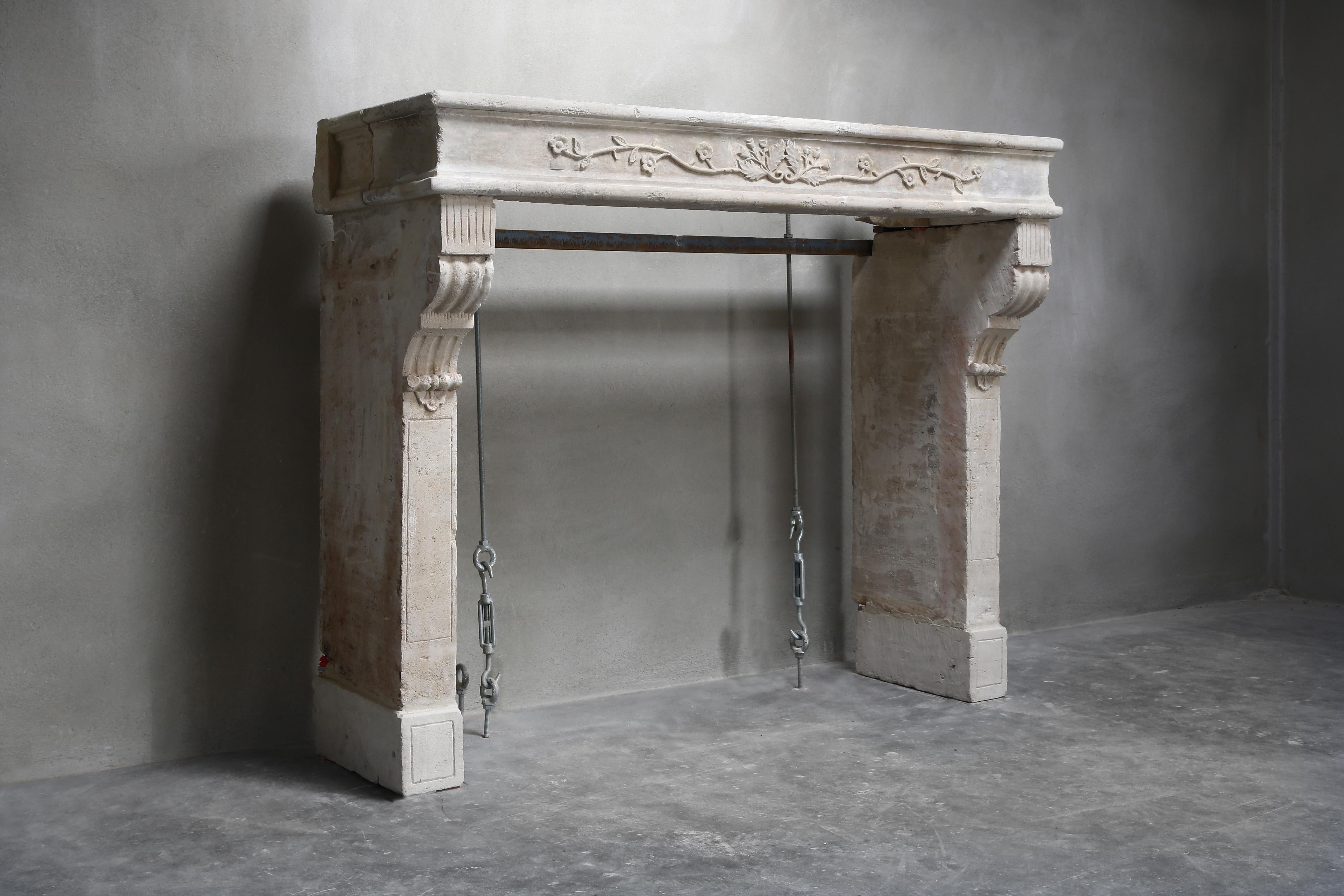 Beautiful decorative antique fireplace of French limestone from the 19th century. The antique fireplace is in the style of Louis XVI and has an ornament with leaves in the middle of the upper part. You can see the cannelures on the legs. An antique