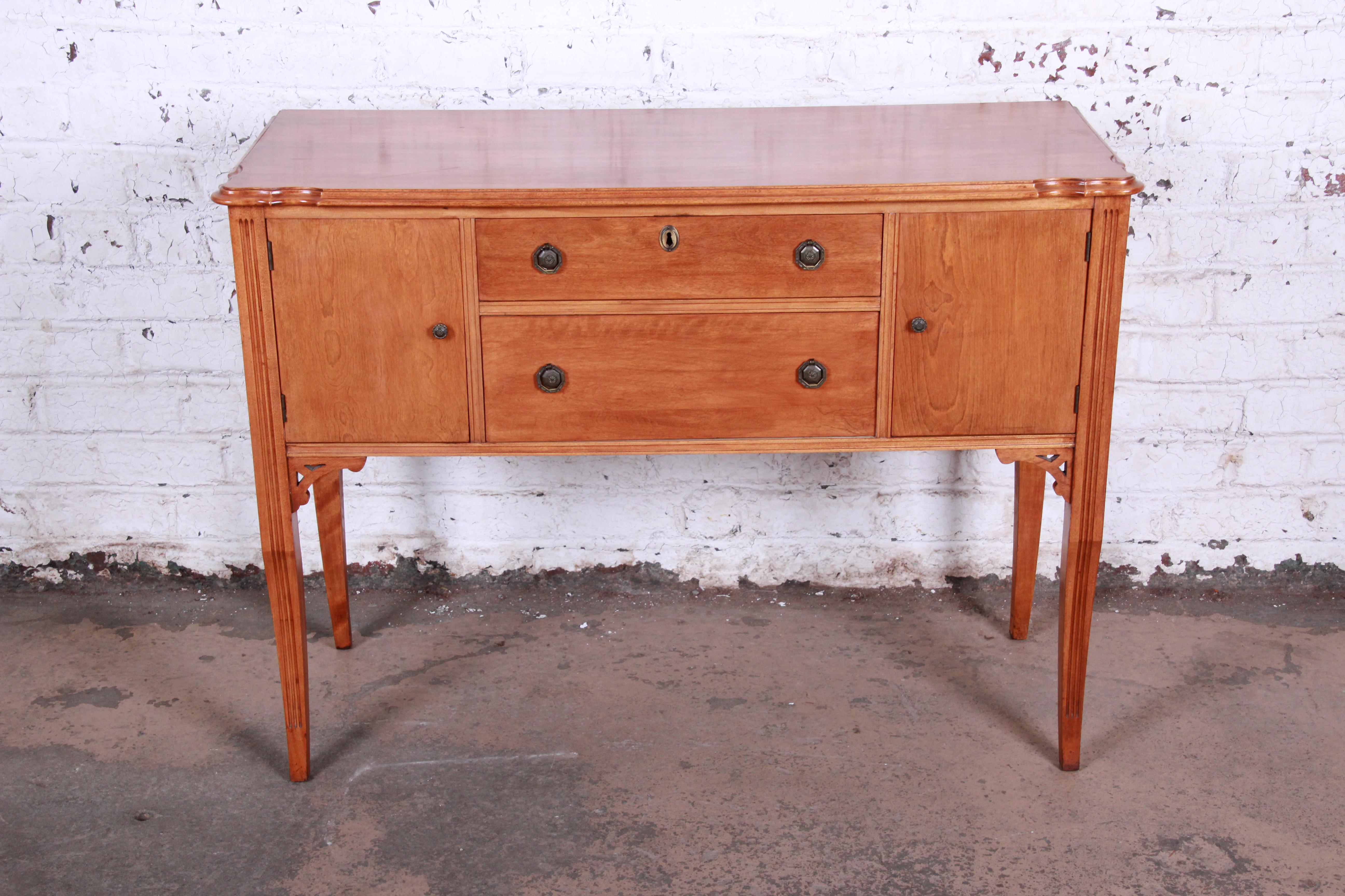 A beautiful antique maple sideboard buffet by S.I. Frank & Son of Chicago. The sideboard features gorgeous wood grain, original brass hardware, and subtle carved wood details. It offers good storage, with two cabinets and two dovetailed drawers. The