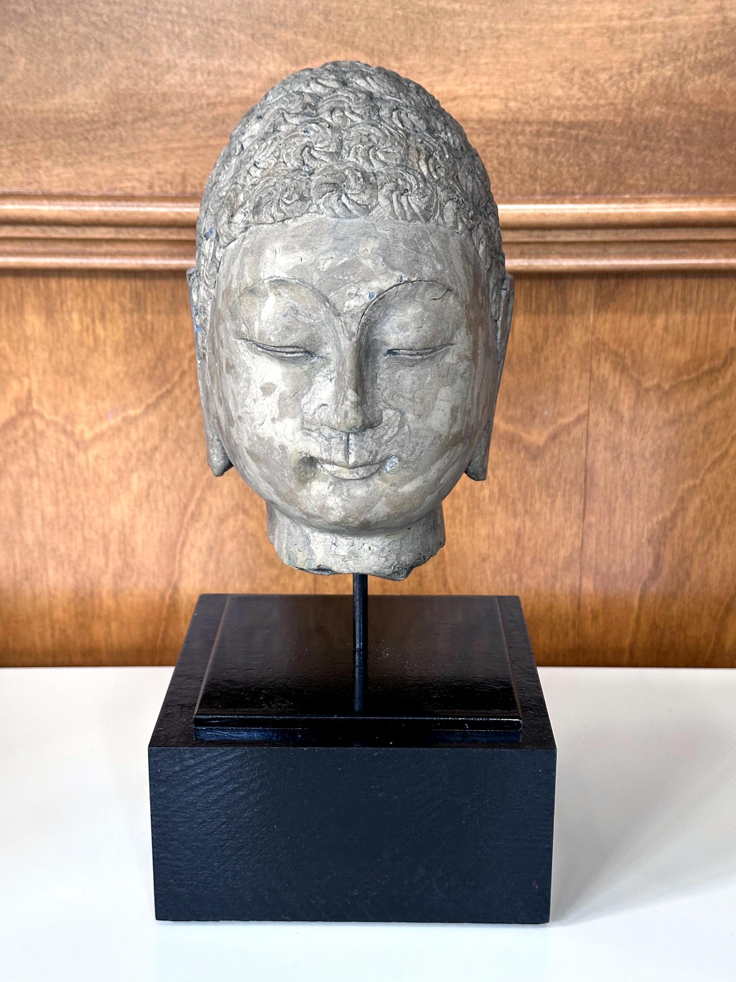 Scolpita in un unico blocco di pietra grigio-marrone (probabilmente di granito), questa testa di Buddha rappresenta lo stile Qi del Nord in Cina (550-577 d.C.) e probabilmente del periodo. Lo stile Qi del Nord è un periodo unico per l'iconografia